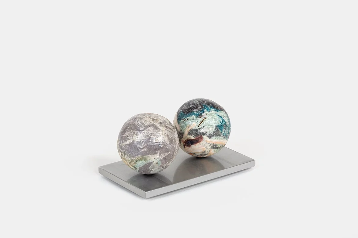 Yasue Maetake Orb Materia—Algae, 2026. Two spherical sculptures on a rectangular aluminum base, the left with soft gray-green mineral surface and the right with blue, black, and brown tones.