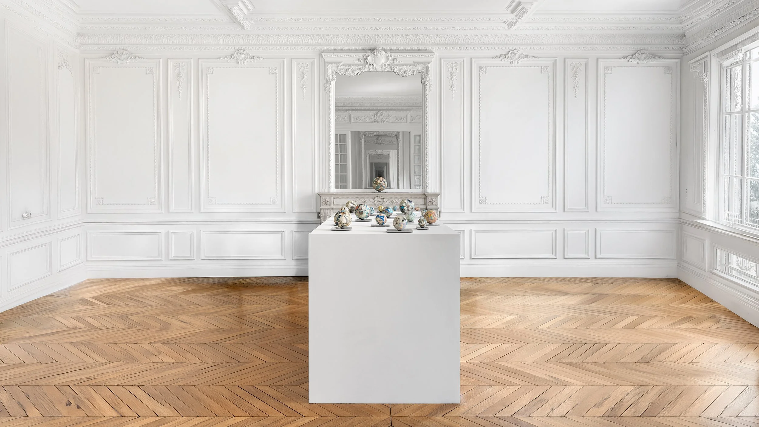Yasue Maetake Orb Materia—Carved Algos gallery installation: centered view of multicolored carved spheres on a white pedestal in a European classical room with wooden floor and infinite mirror reflections