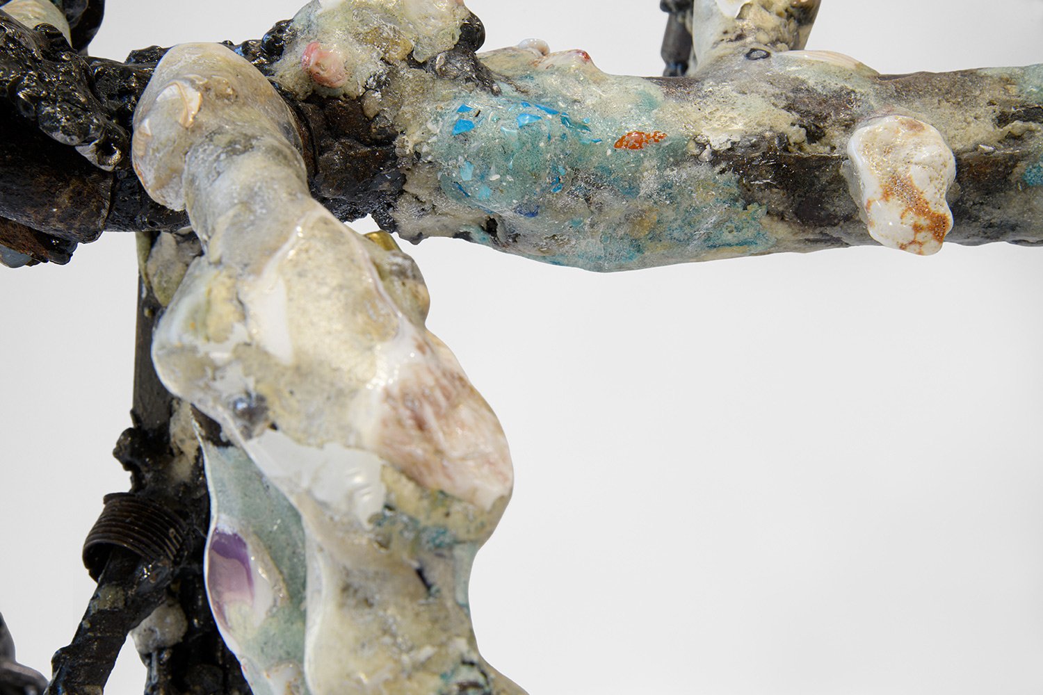 Yasue Maetake's sculpture Mare Fecunditatis – resurrection, 2025. Close-up detail of the hybrid surface showing prominent shiny dark metallic elements intertwined with rough, porous white and gray organic forms and patches of multicolored glazes.