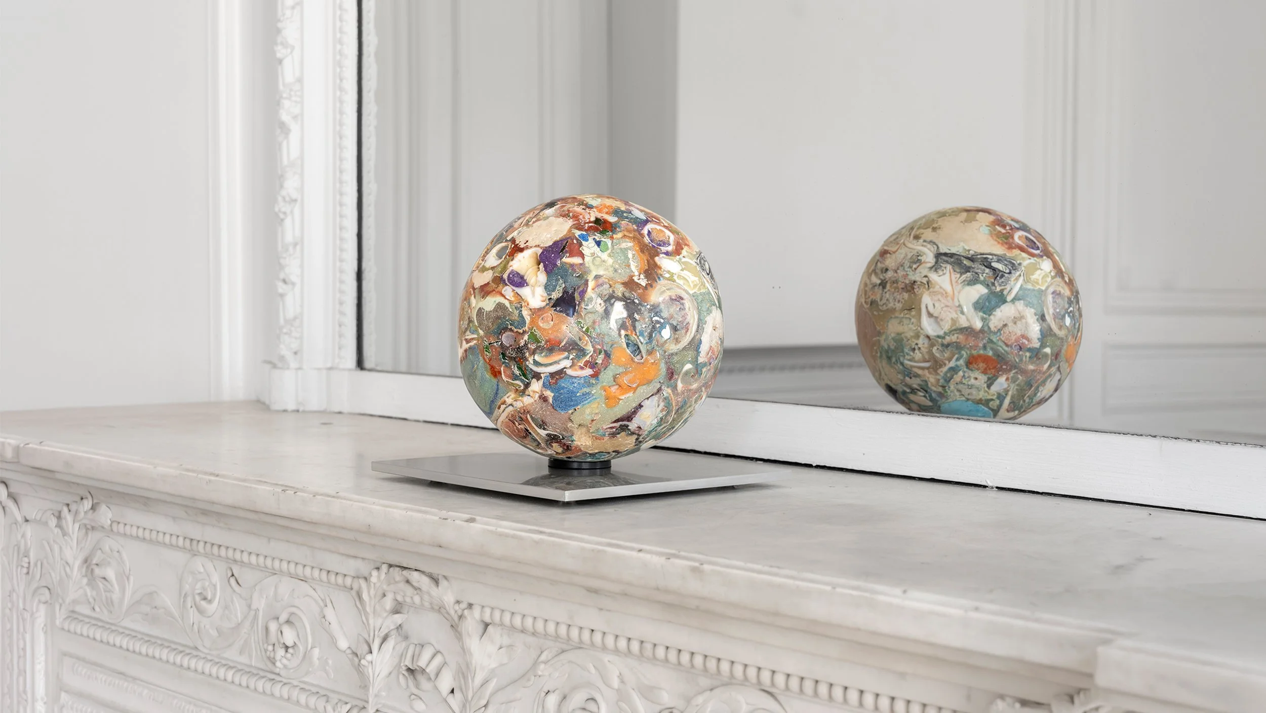 Yasue Maetake Orb Materia—Carved Algos: carved multicolored sphere on a square aluminum base placed on a marble fireplace mantel, reflected in a large mirror in a European classical interior