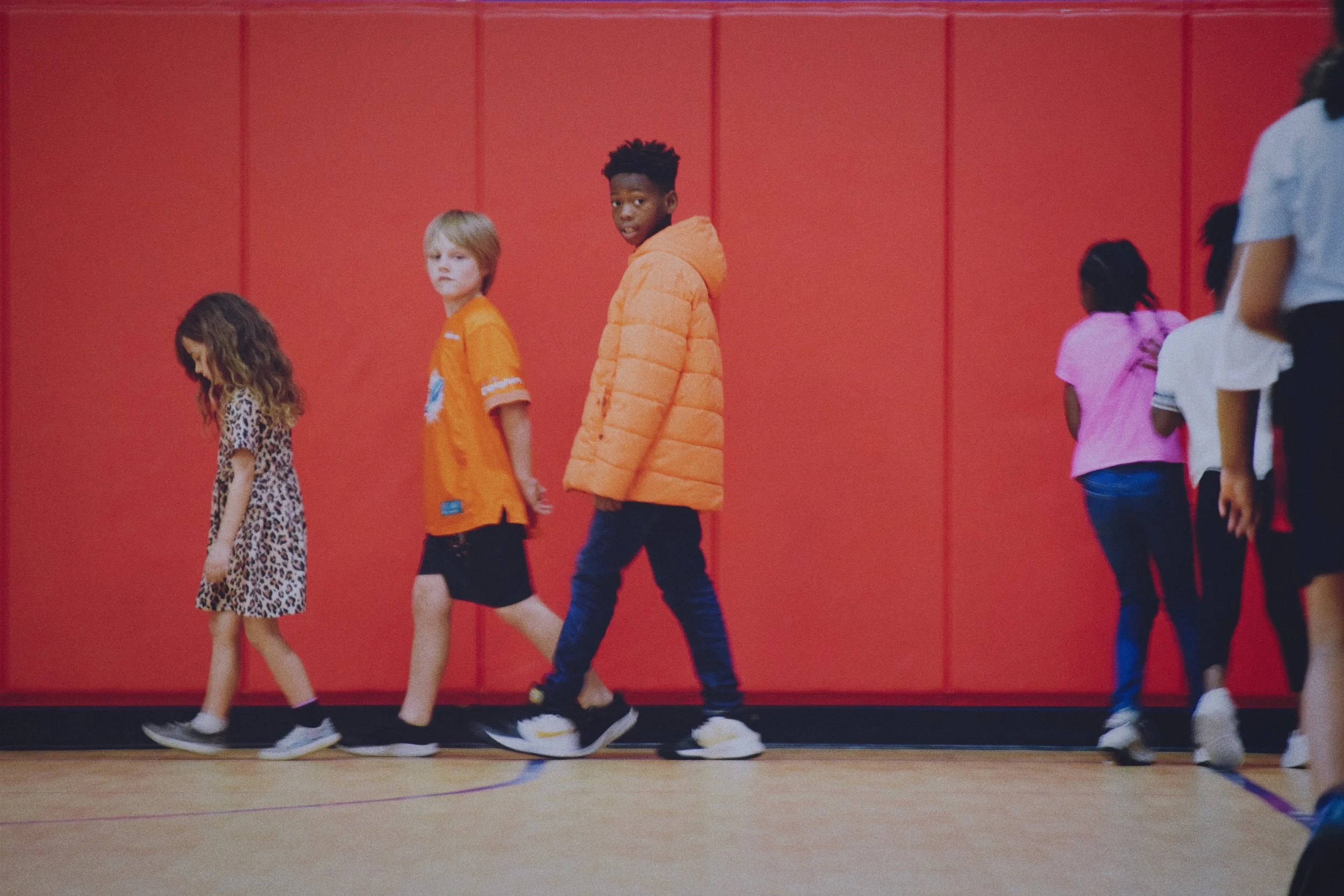 Children at Boys & Girls Club in St. Augustine walking in a line in a gymnasium with a red padded wall in the background.