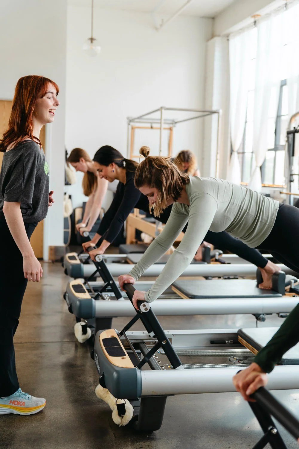 Women participating in a reformer Pilates class, doing exercises on Pilates reformer machines with an instructor supervising.