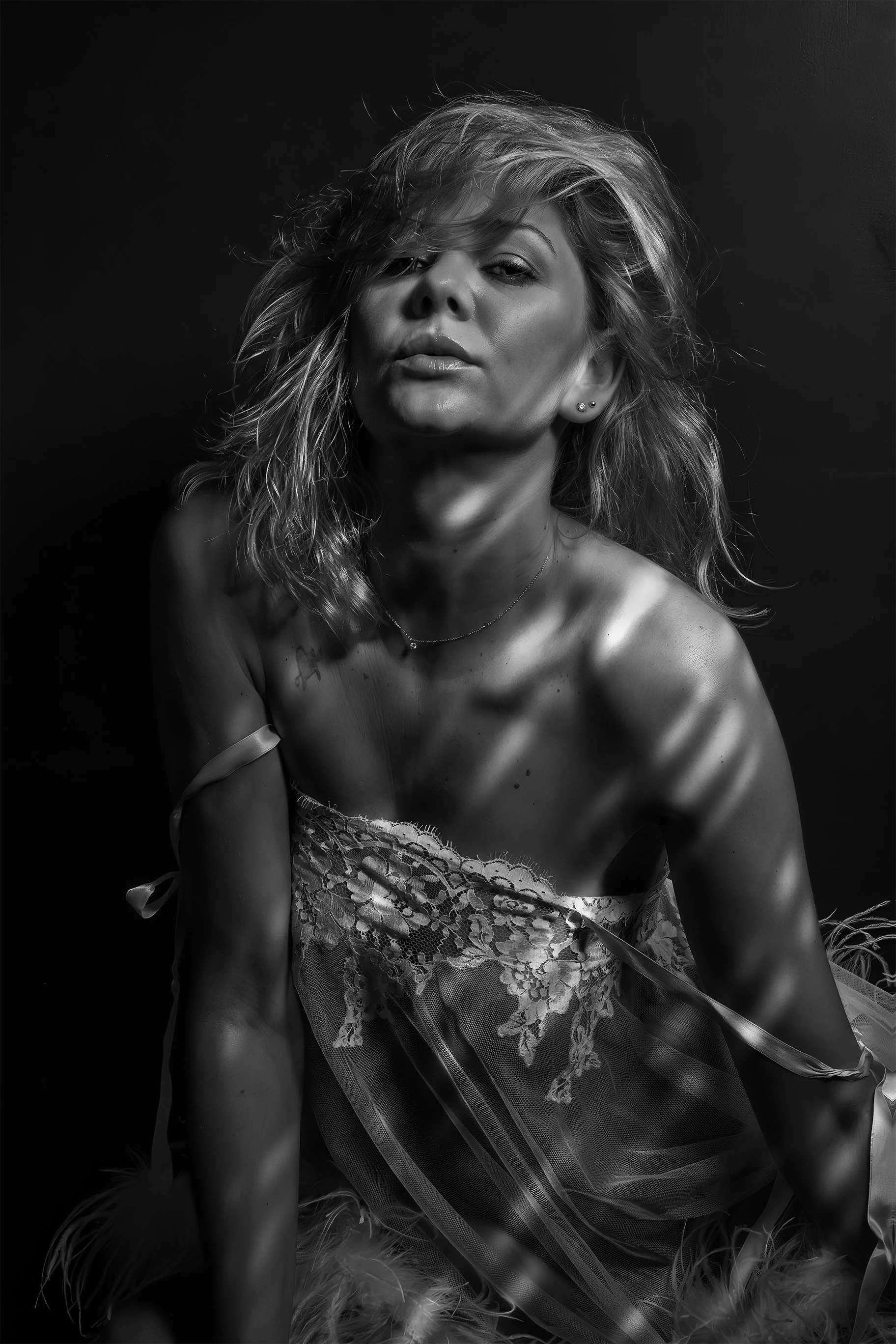 Black and white portrait of a woman with wavy hair, wearing a lace and tulle dress, with shadows cast across her face and body.
