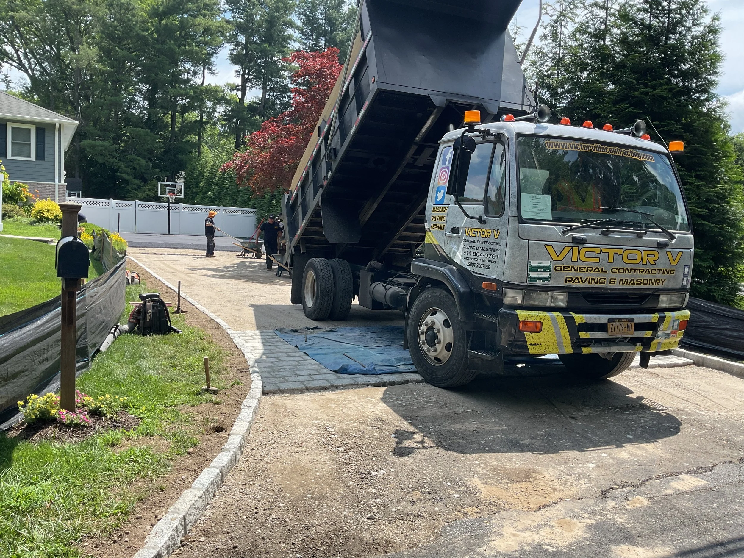 A paving truck and workers installing a new driveway in a residential yard.