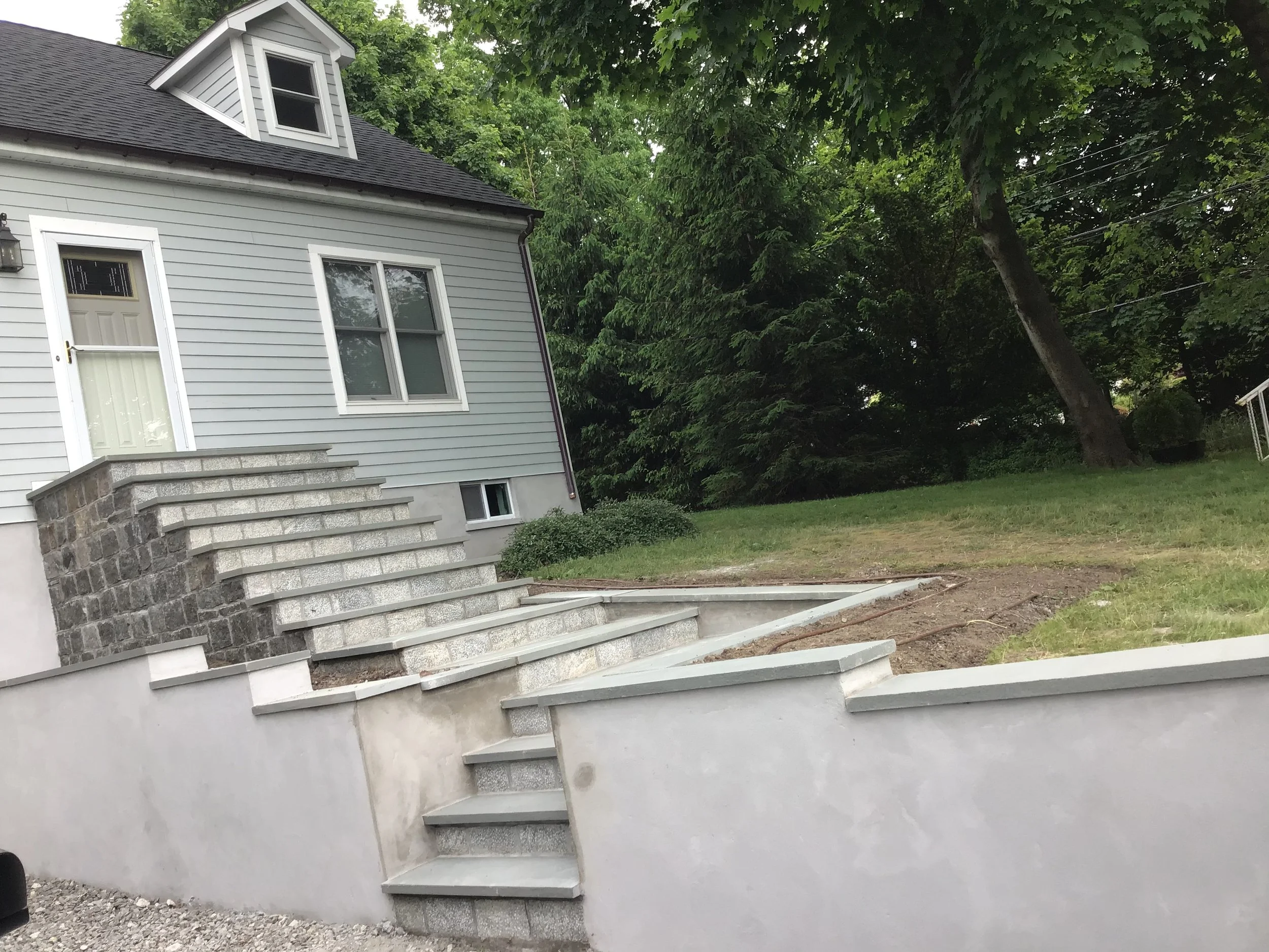 Front of a house with a stone staircase leading up to a white door, and a lawn with trees in the background.