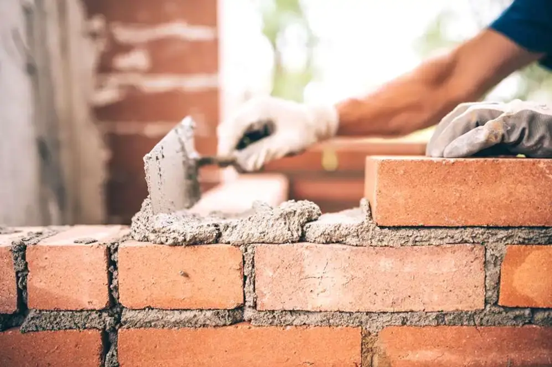 Close-up of a bricklayer laying bricks on a wall, using a trowel to apply mortar.