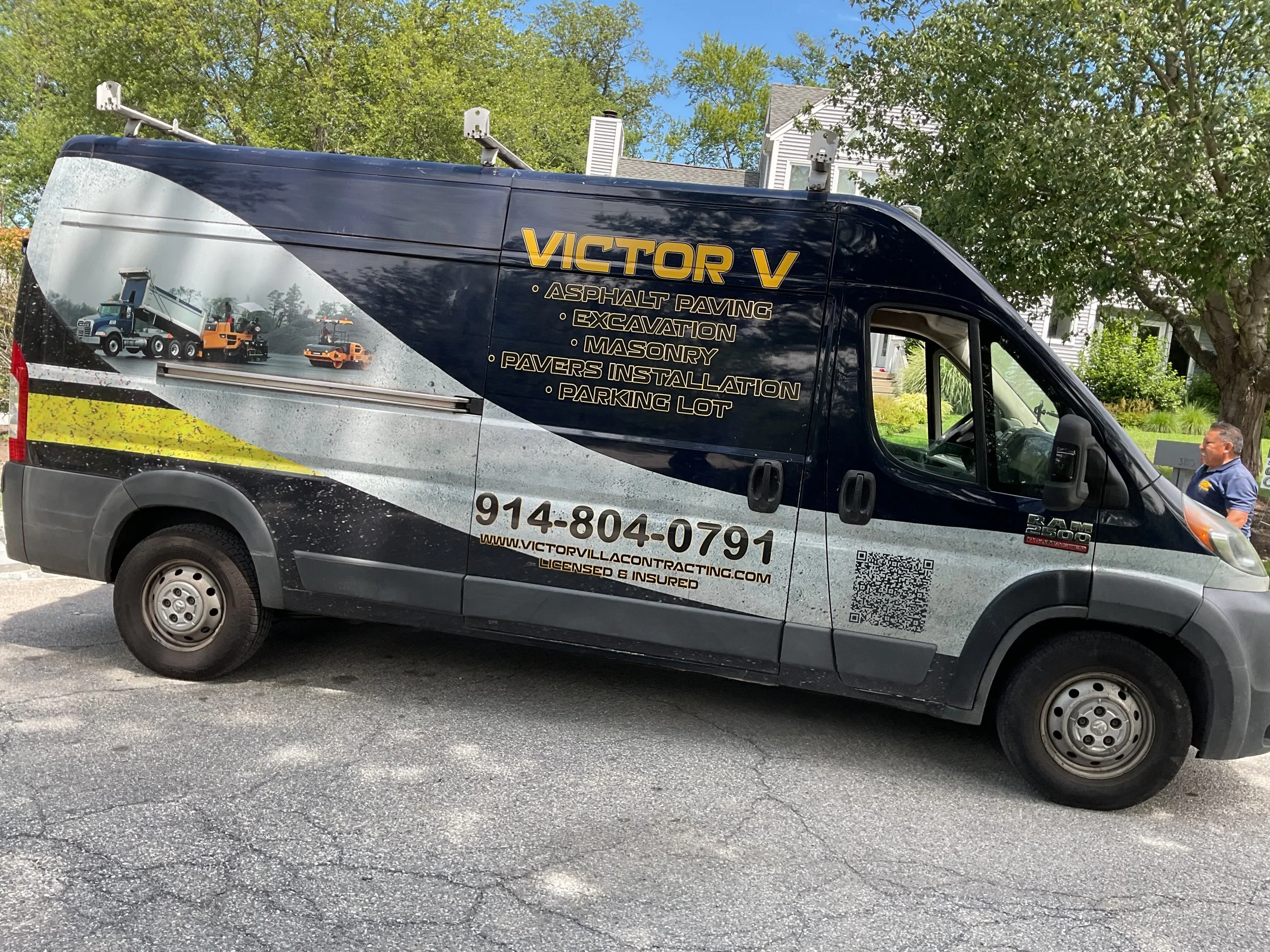Black commercial van with graphics and yellow text advertising Victor Villa Mason Contracting services including asphalt paving, excavation, masonry, pavers installation, and parking lot work. The van displays a phone number, website, and QR code.