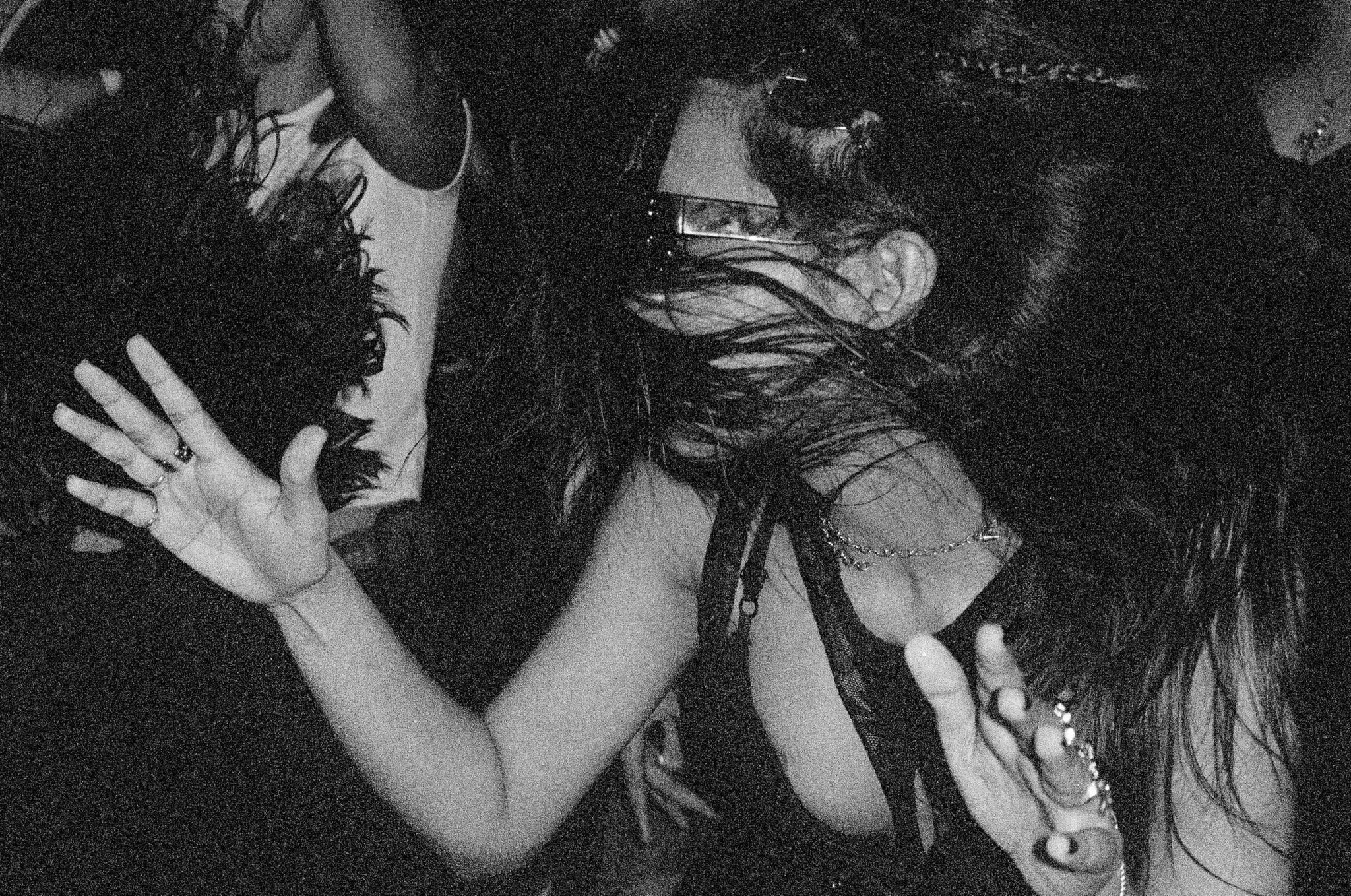 Two women dancing closely, one wearing dark glasses and the other with long wet hair, in a dark setting.