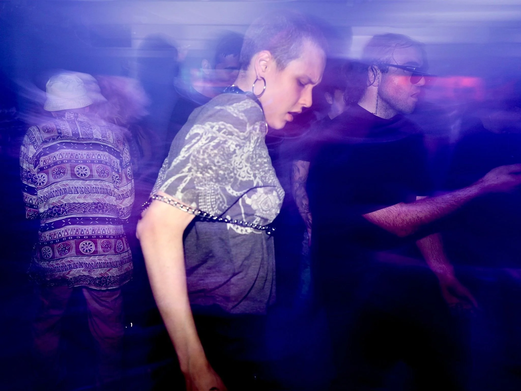 People at a nightclub dance with colorful lights and motion blur.
