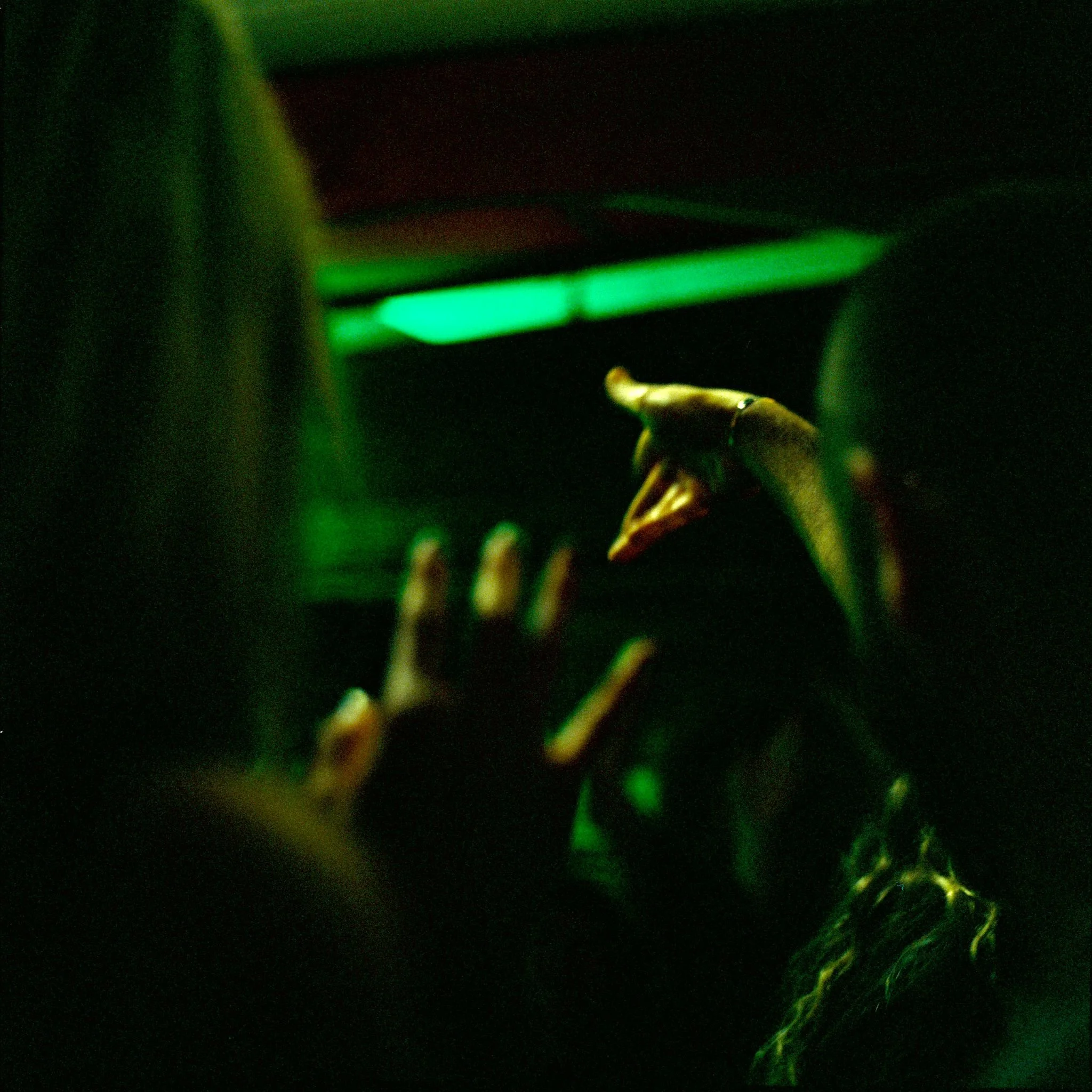 A person reaching towards a landscape with a dinosaur figure illuminated by green lighting, seen from behind in a dark setting.