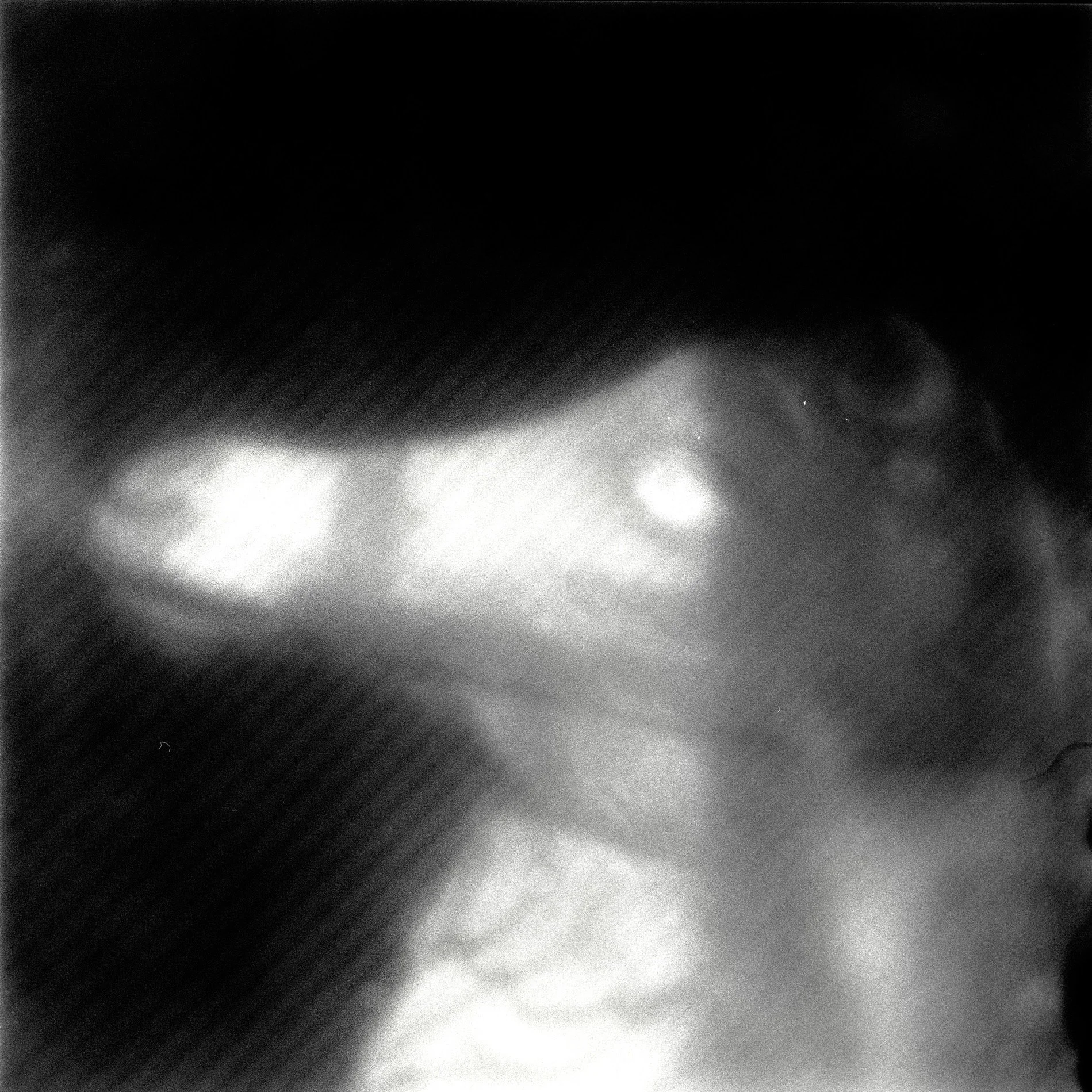 A black and white abstract photograph with blurred shapes and light spots, creating a sense of motion and mystery.