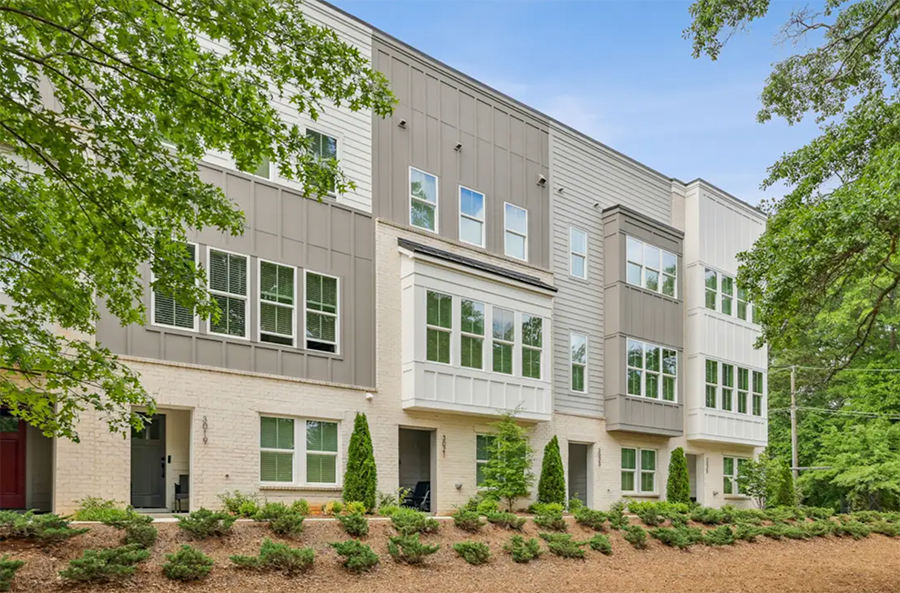 Exterior view of a modern multi-floor apartment building with large windows and surrounded by green trees and landscaped shrubbery.