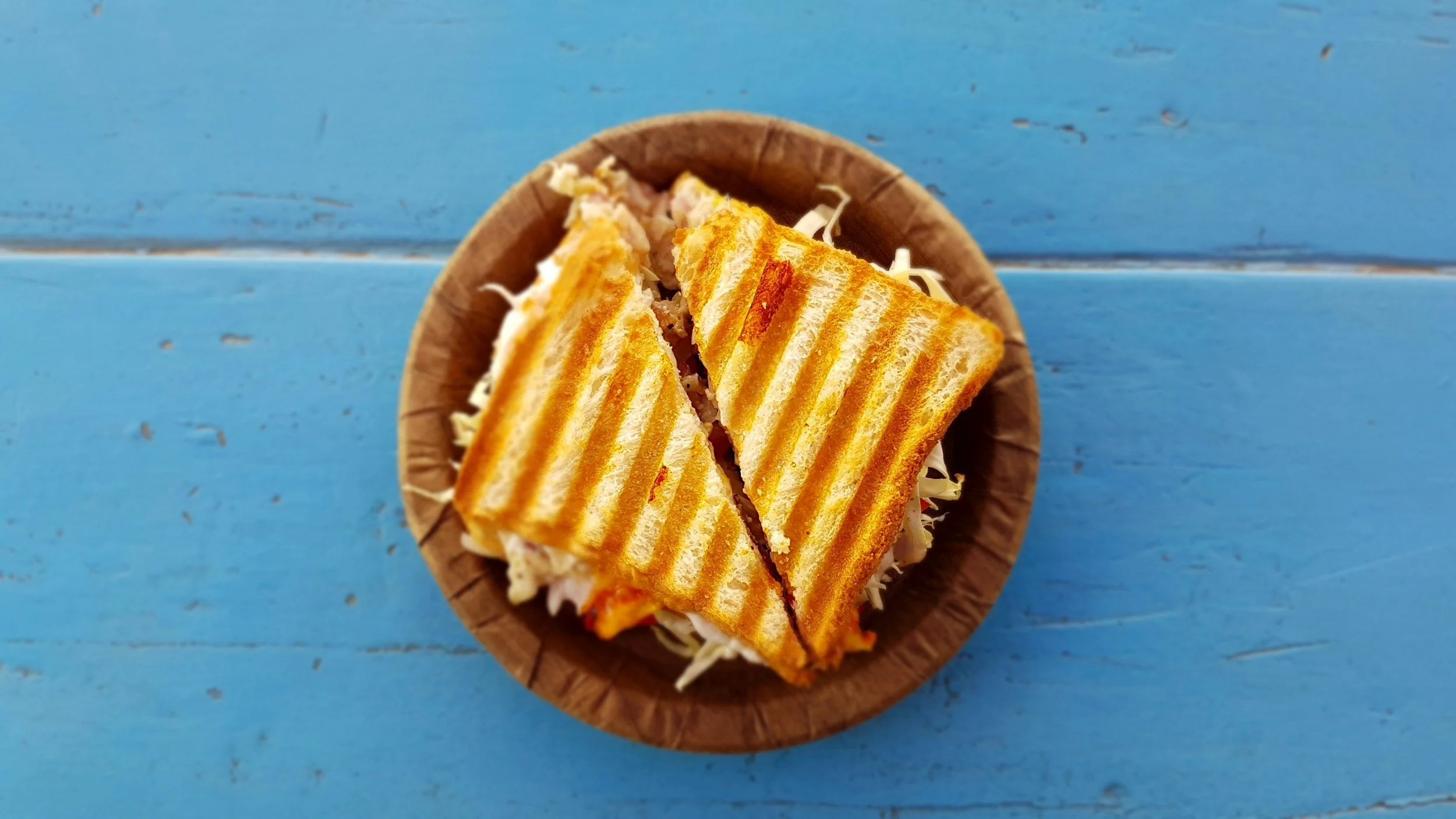 Grilled sandwich with visible cheese, cut into two triangles, served in a wooden bowl on a blue wooden surface.