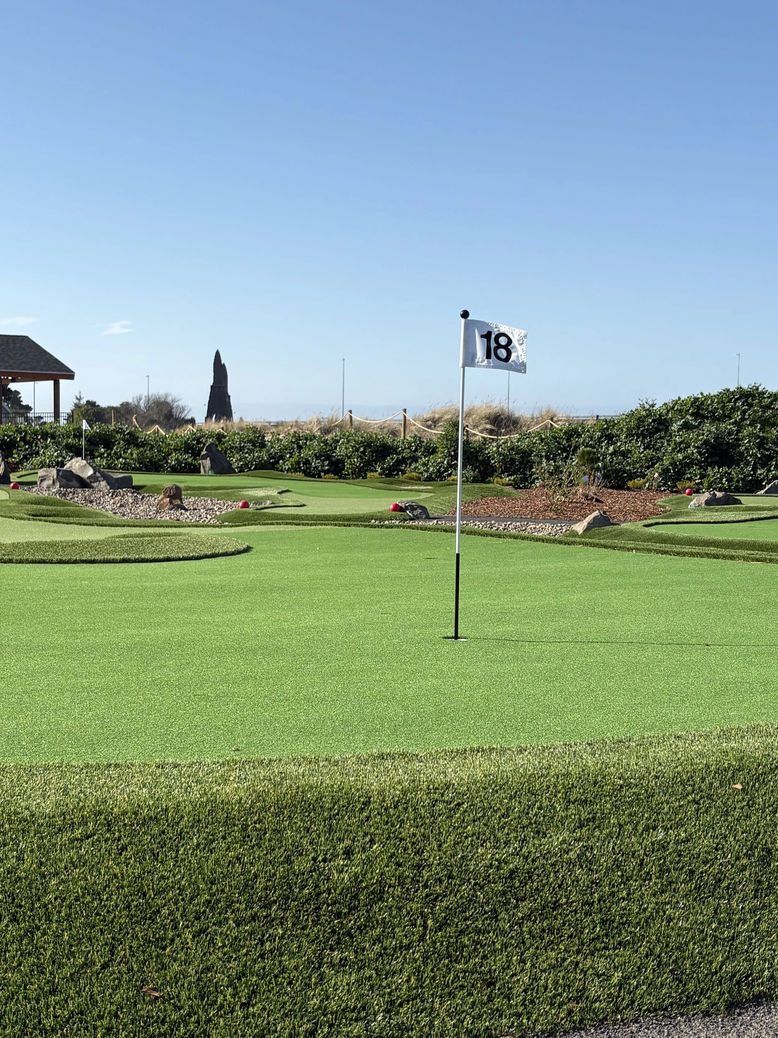 A miniature golf green with a white stick and the number 18 on the flag