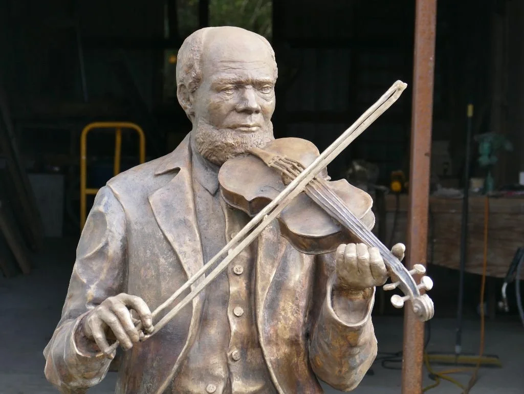 Bronze statue of a man playing the violin, with a beard and dressed in a suit.