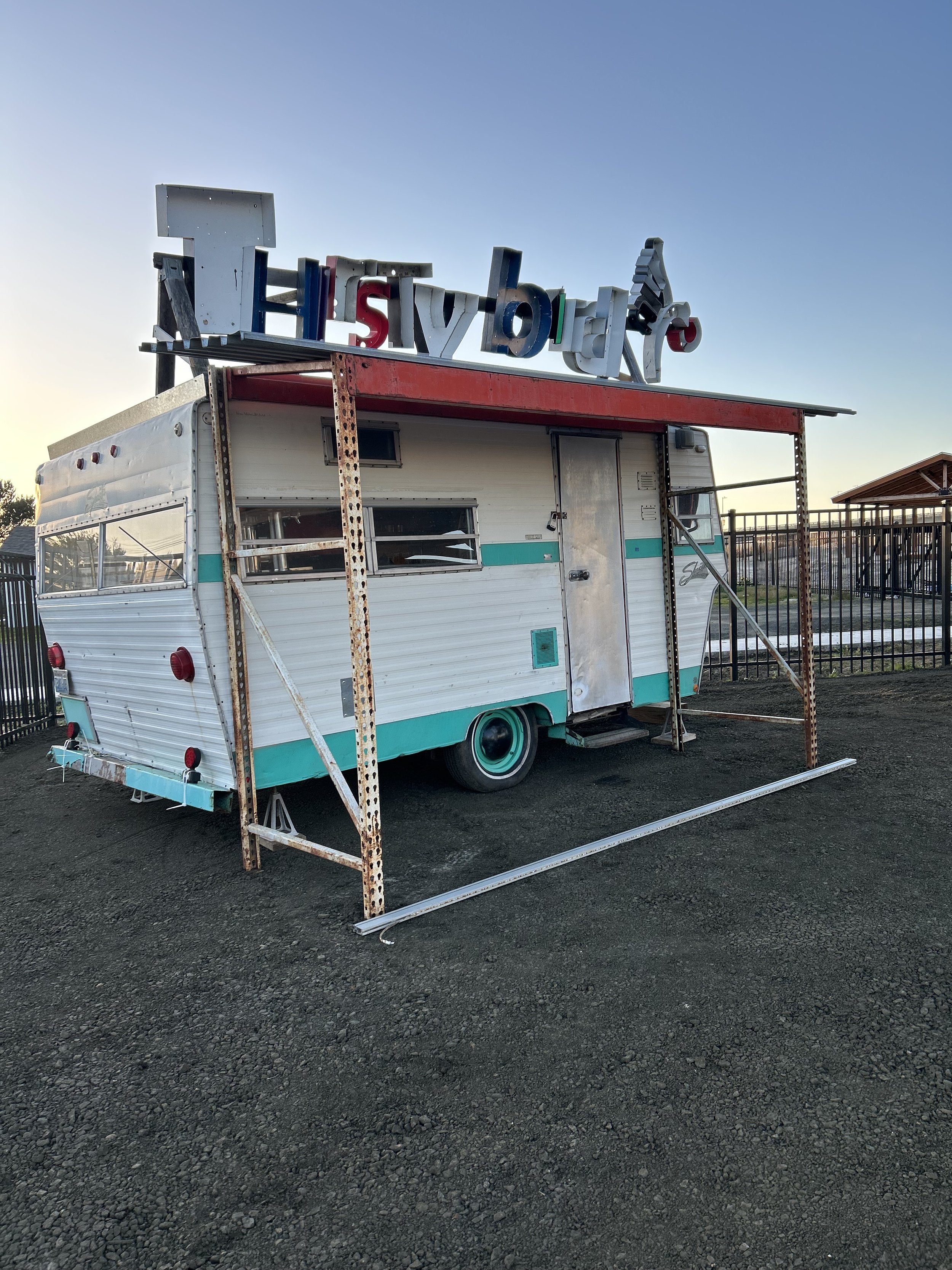 Vintage trailer with scrap metal lettering spelling Thirsty Bird sun setting in the background