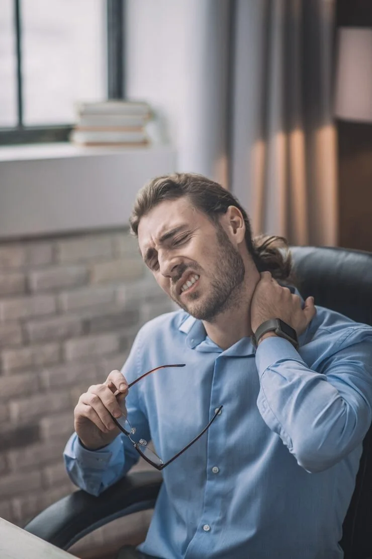 man in blue shirt rubbing neck appearing to be in pain