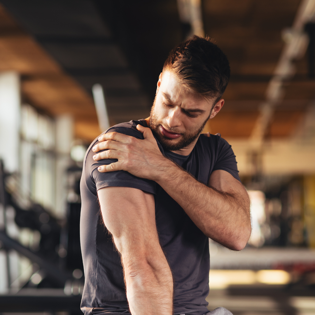 man in a gym holding his shoulder from pain