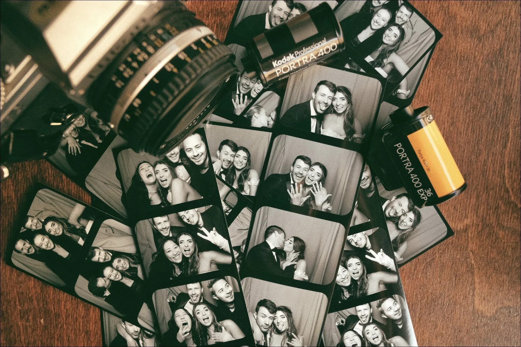 A collection of black-and-white photo booth pictures showing smiling and laughing people, along with a roll of Kodak professional Portra 400 film, all placed on a wooden surface.