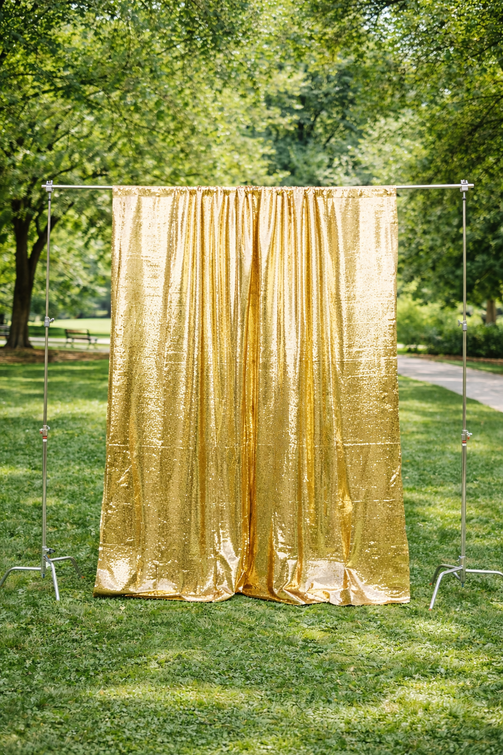 Golden shiny curtain hanging on a metal frame in a park with green trees and grass.
