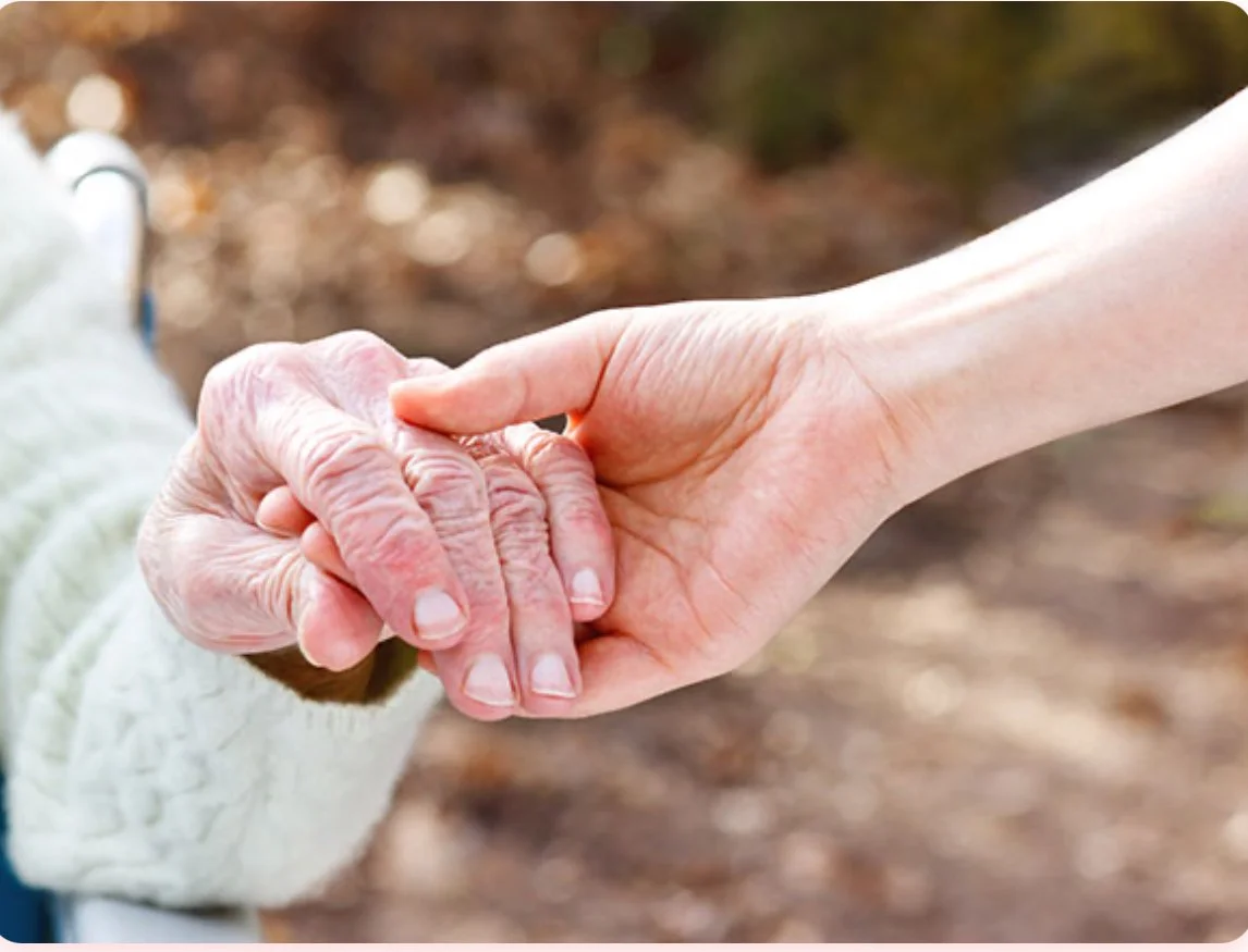 An elderly person's hand holding a younger person's hand outdoors.