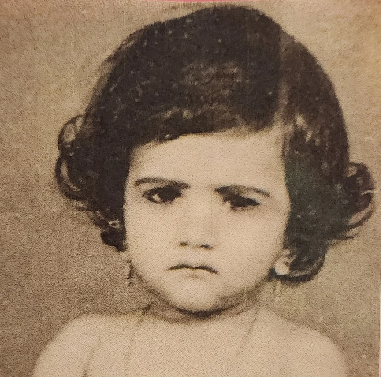 Black and white photo of a young child with curly hair, one eye closed, making a facial expression.