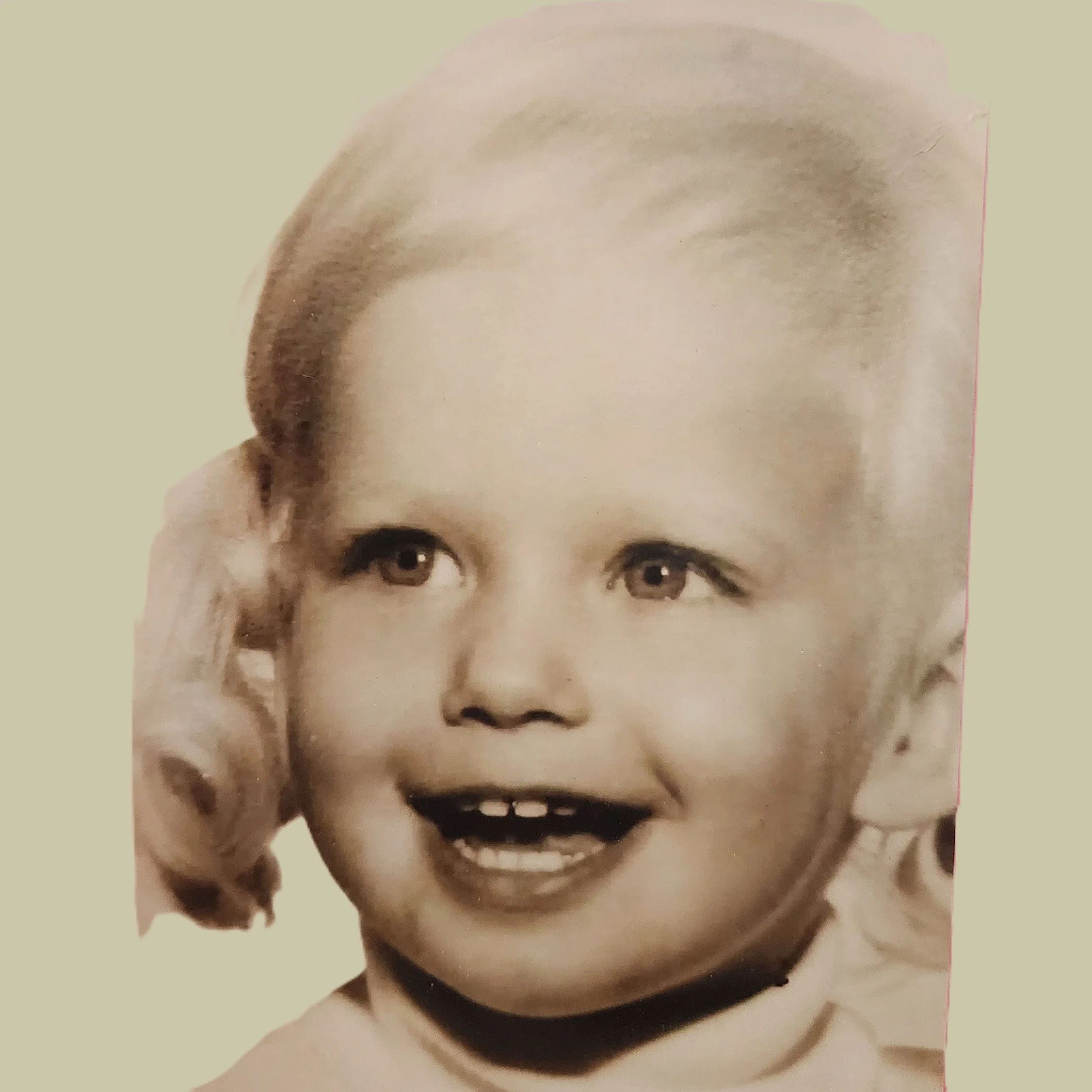 Close-up of a vintage black-and-white photograph of a young girl with a big smile, showing missing front teeth, with curly hair and bright eyes.