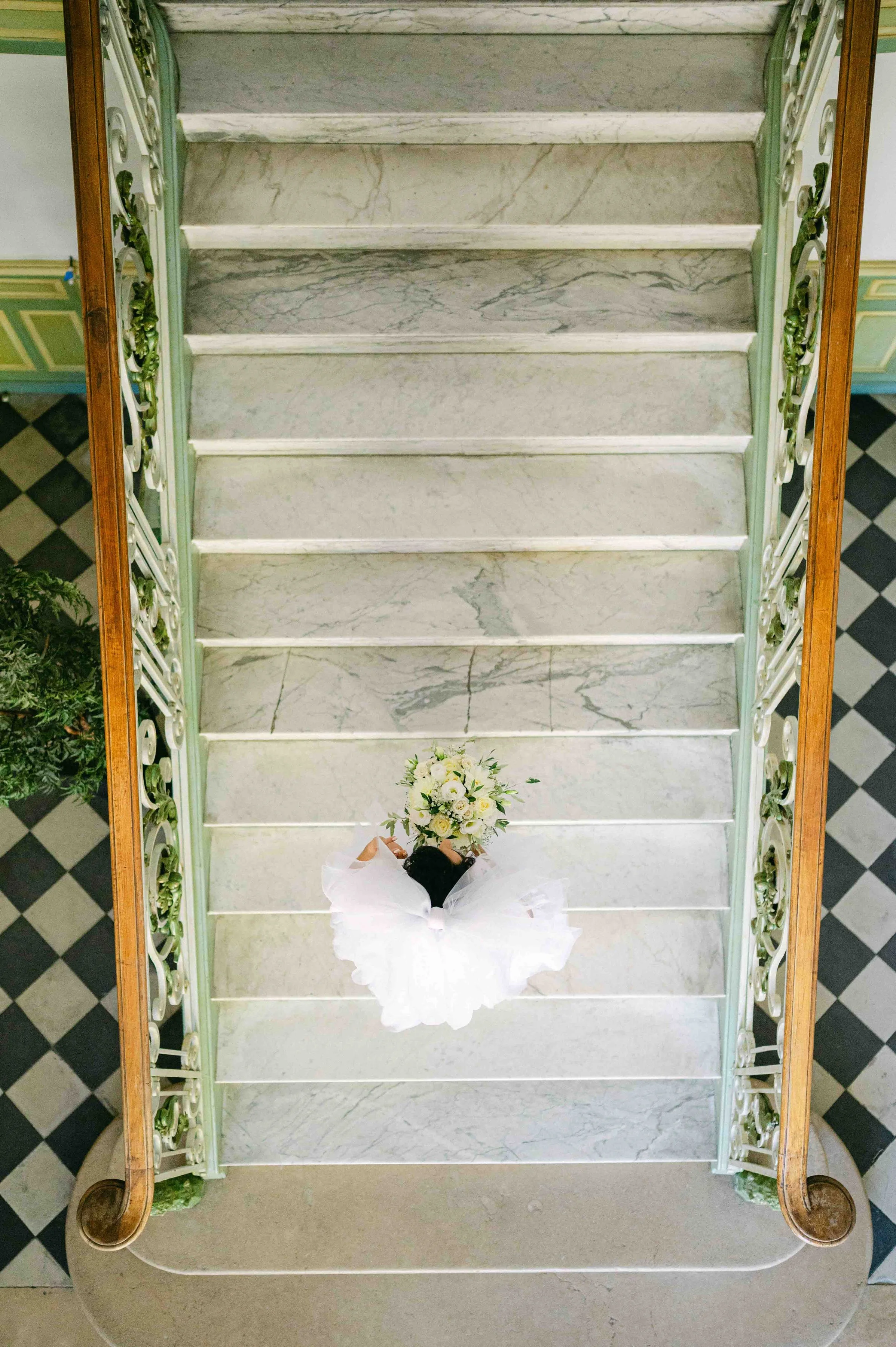 Une vue aérienne d'un escalier en marbre style provençal avec une mariée portant une robe blanche et tenant un bouquet de fleurs à la main. Elle se rend à la mairie pour son mariage.