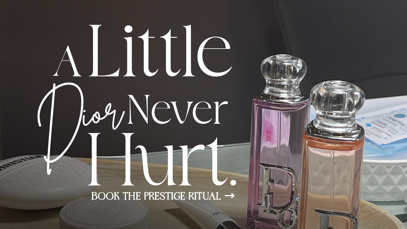 A wooden tray holding two Dior perfume bottles with clear glass caps, a white soap dish, a wrapped packet, and a tube of product. The background features a dark surface and text reading 'A little Dior never hurt. Book the prestige ritual.'