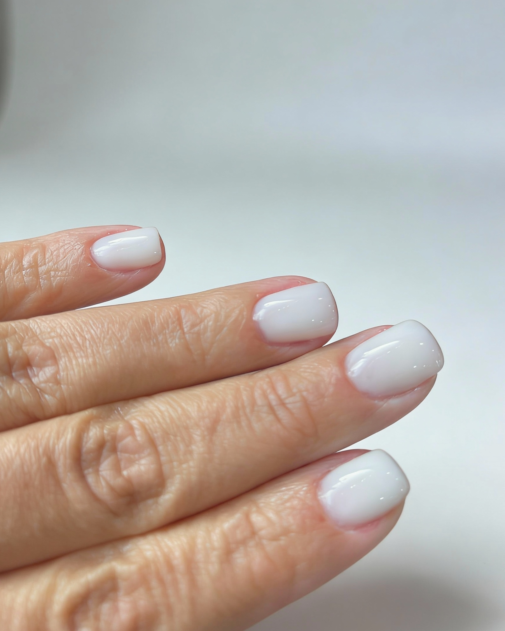 Close-up of a hand displaying neatly manicured nails painted with white nail polish against a light background.