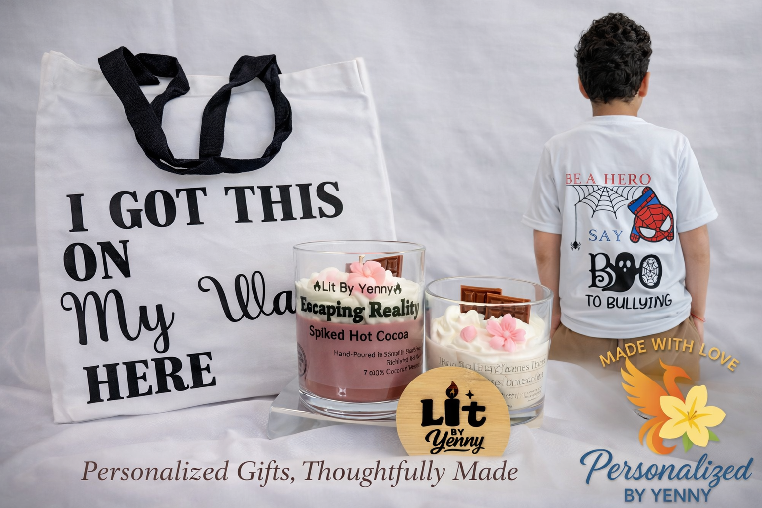 White tote bag with black handles and text reading "I GOT THIS ON MY WALL HERE," two candles labeled "Lit By Yenny" and "Escaping Reality" with pink flowers and chocolate, a boy wearing a white T-shirt with superhero-themed design and text, and a yellow logo with a redbird and flower with text "Made With Love."