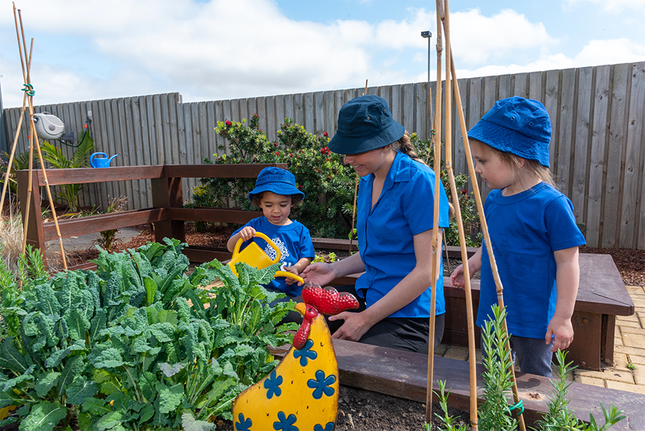 Highfields Central Educator and children water the vegetable patch