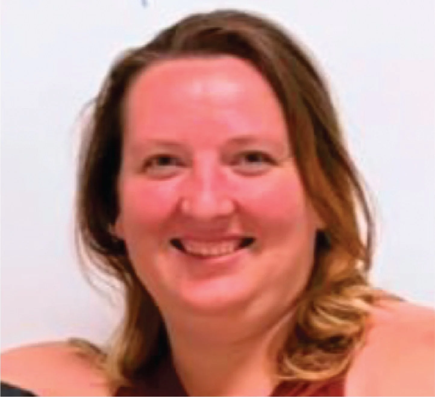 Close-up of a smiling woman with shoulder-length light brown hair against a light background.