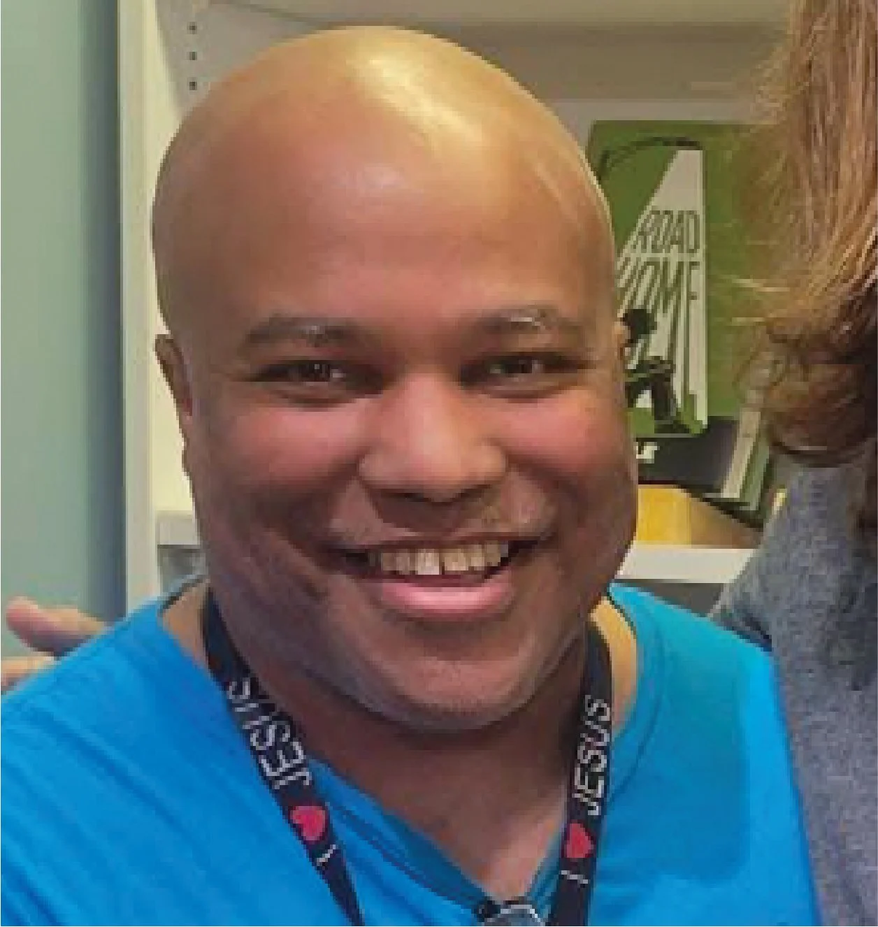 Close-up of a smiling man with a shaved head wearing a blue shirt and a black lanyard around his neck.