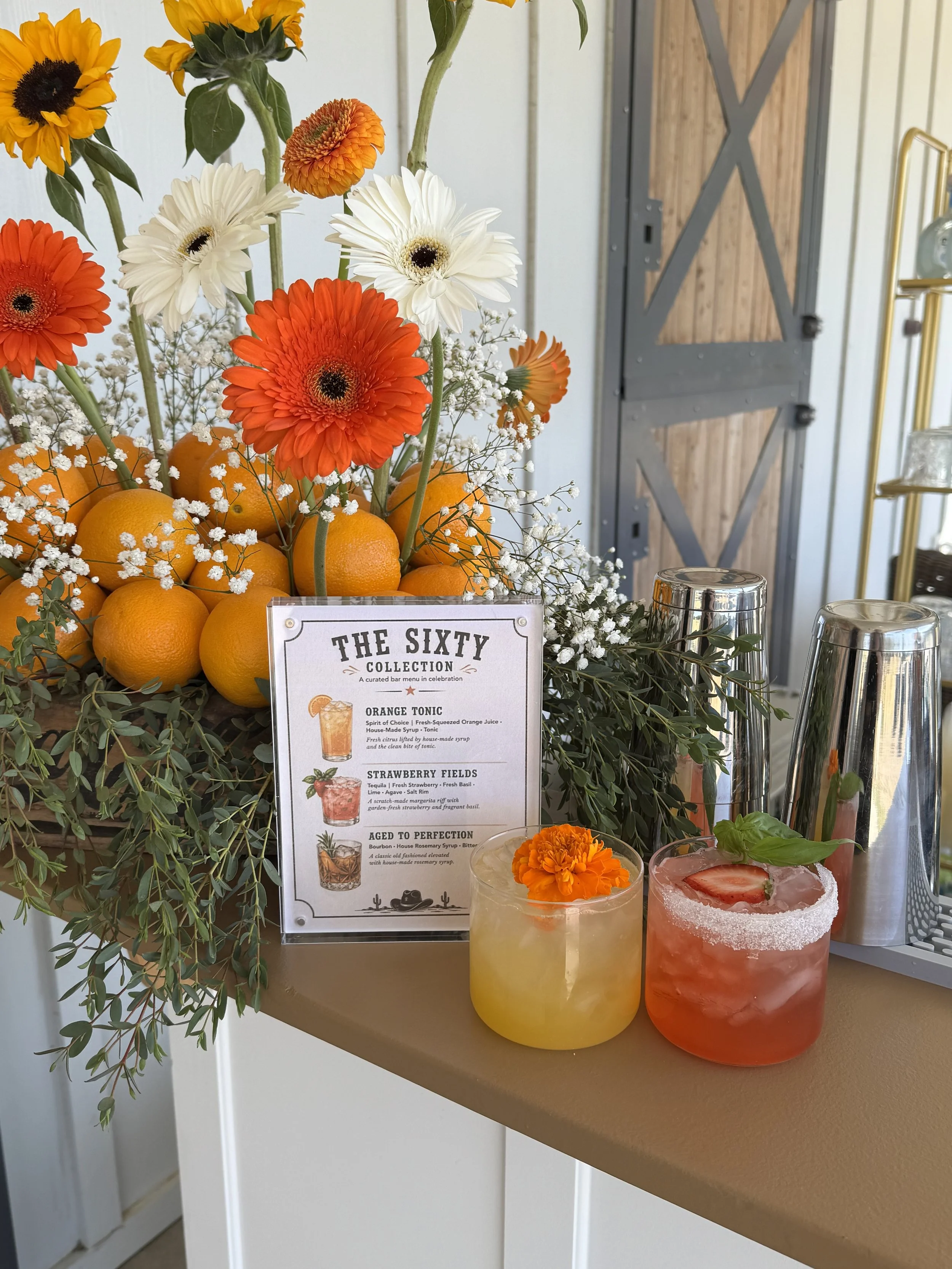 Fresh-pressed cocktail bar served at a 60th birthday party in Orange County, CA. Custom seasonal drink menu featuring signature cocktails, styled orange floral bar display, and full bar setup by BUBBLES Mobile Bar.