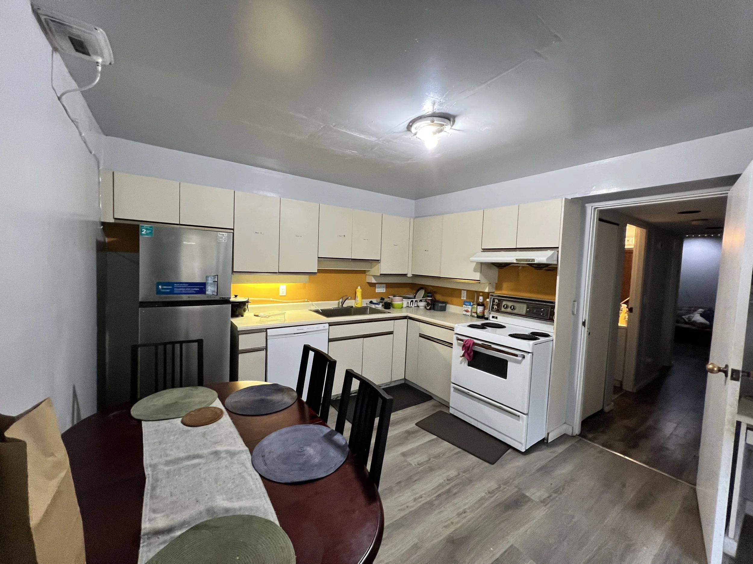 Kitchen with beige cabinets, white appliances, and a dark wood dining table with six chairs and placemats.