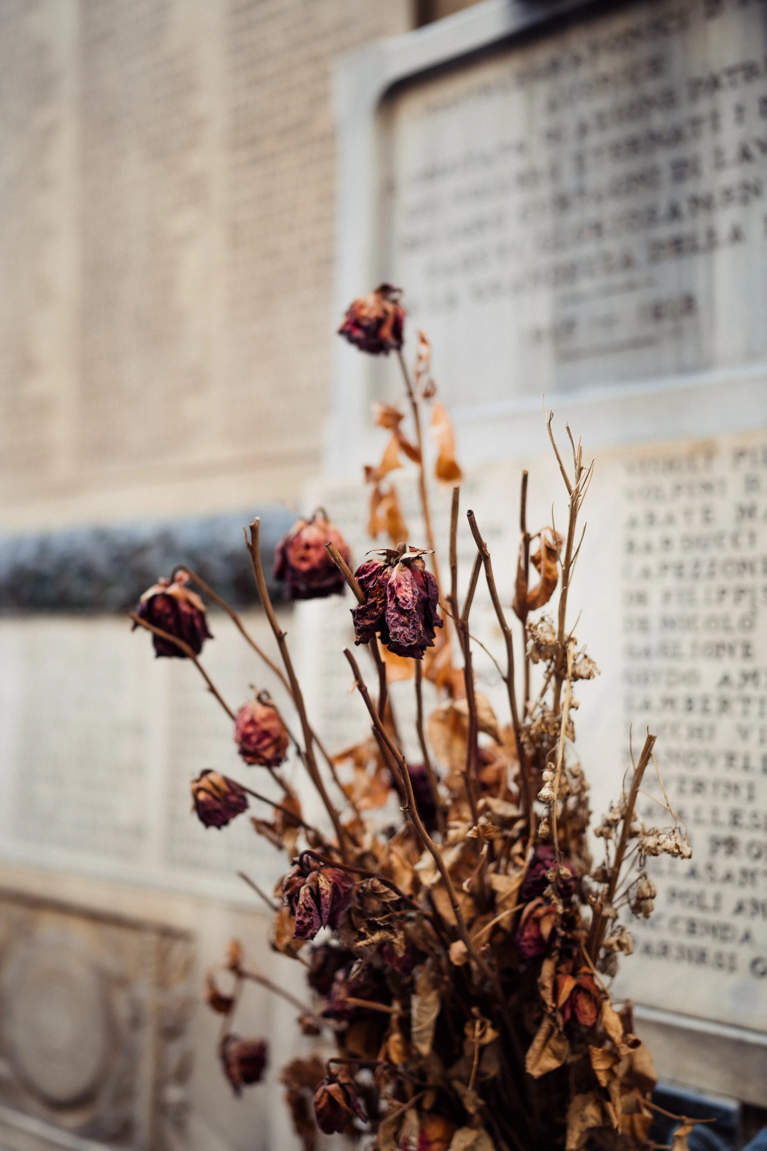 Dried flowers placed in front of a stone engraved memorial plaque.