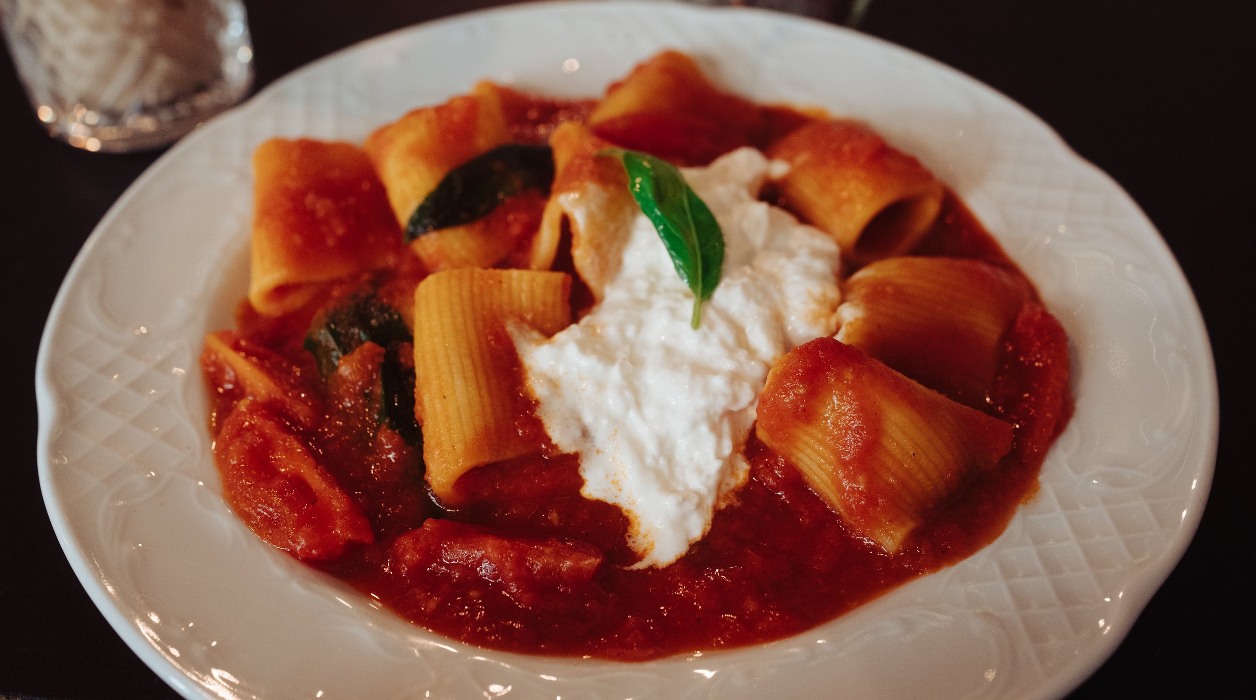 Plate of baked pasta with tomato sauce, topped with ricotta cheese and a basil leaf