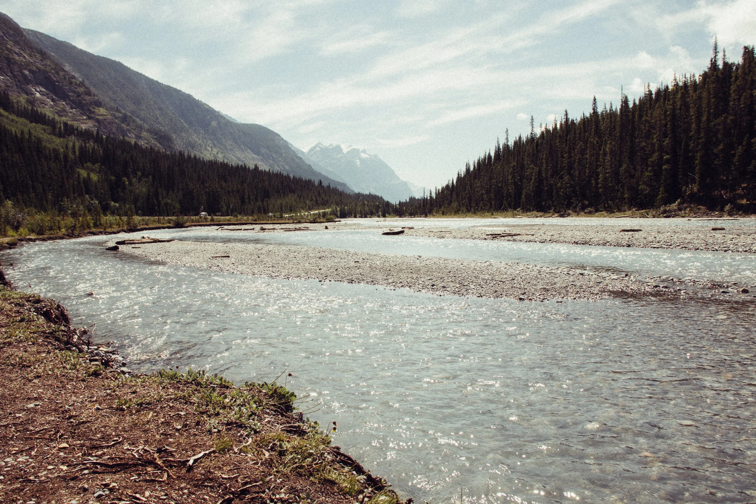 Scenic view of a river flowing through a forested mountain valley under a partly cloudy sky.