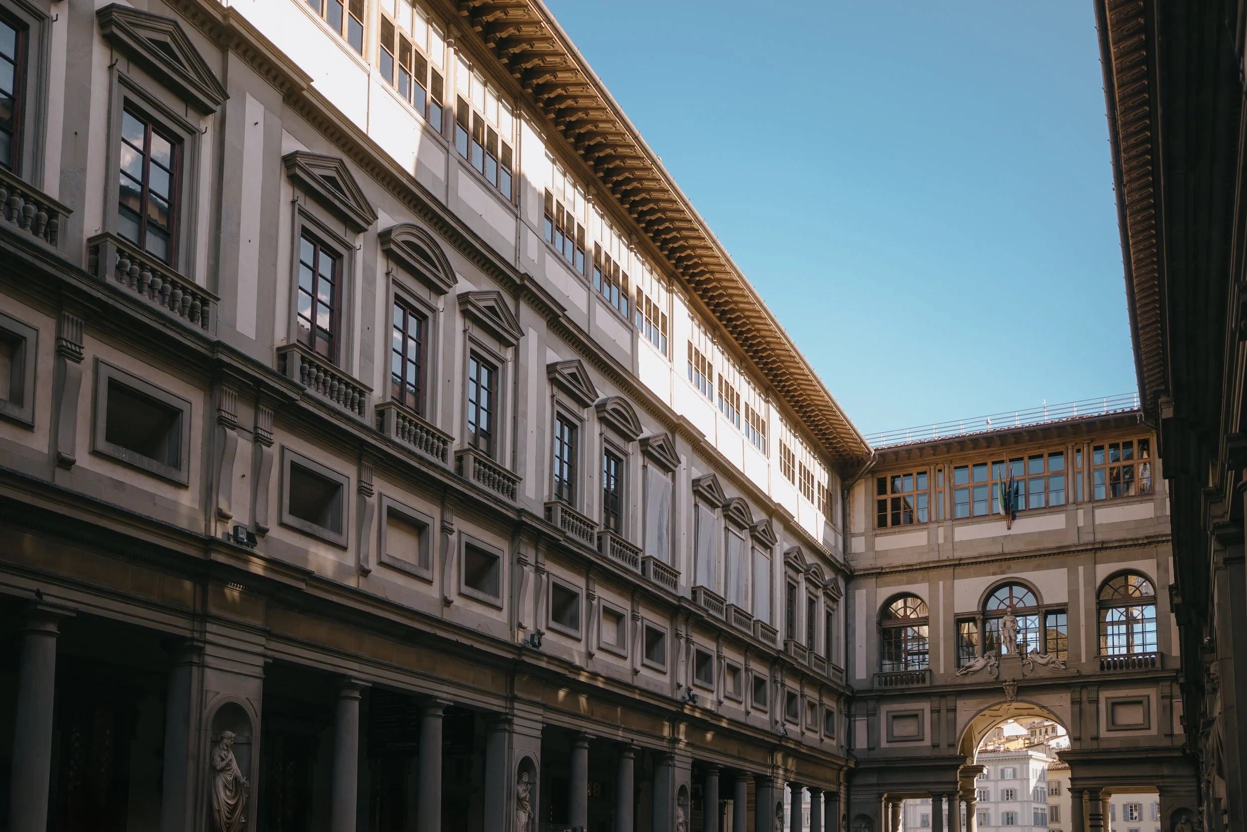 View of an ornate European-style building with multiple stories, large windows, statues, and an archway, under a clear blue sky.