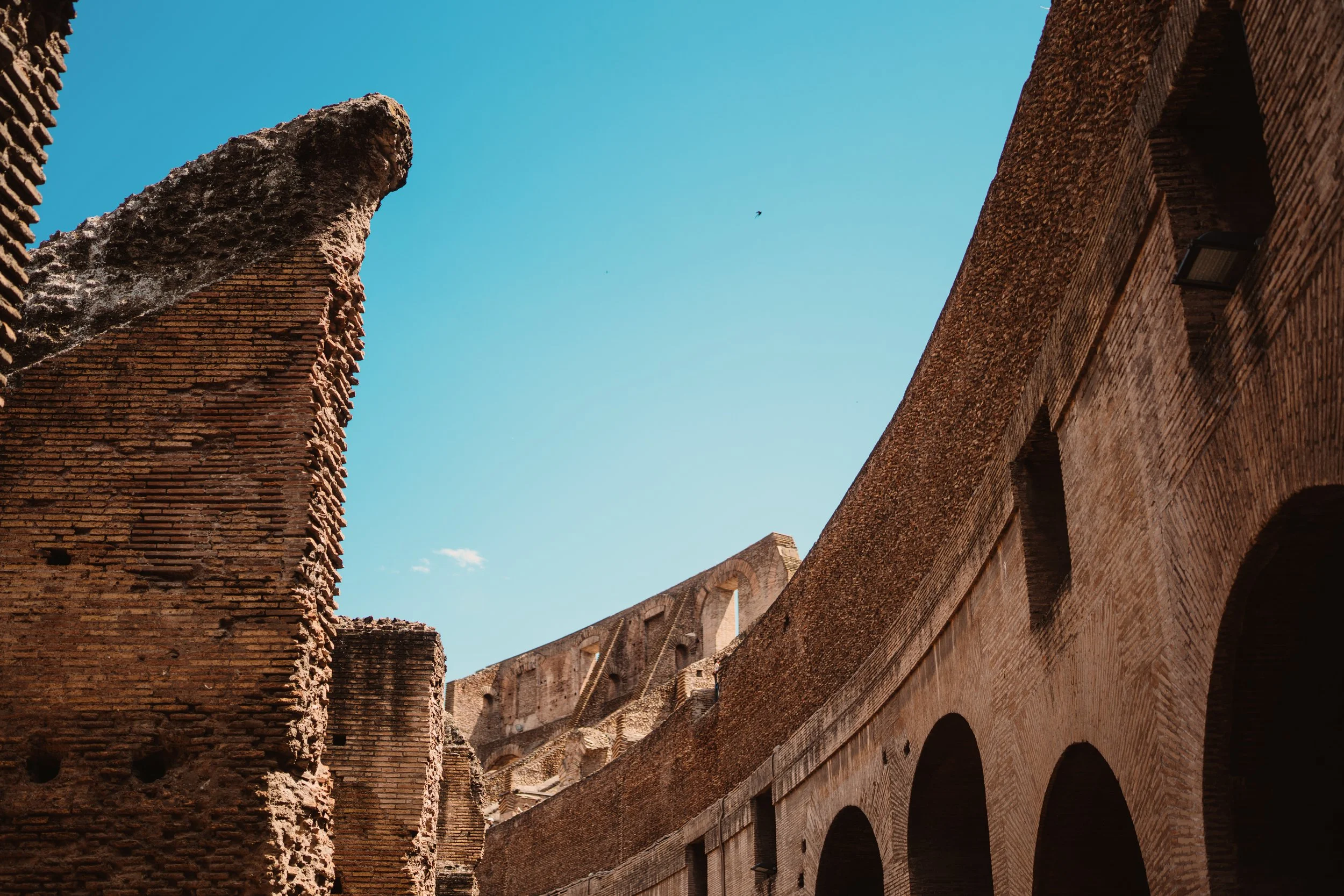 Ancient brick ruins of the Colosseum with arches and a clear blue sky overhead.