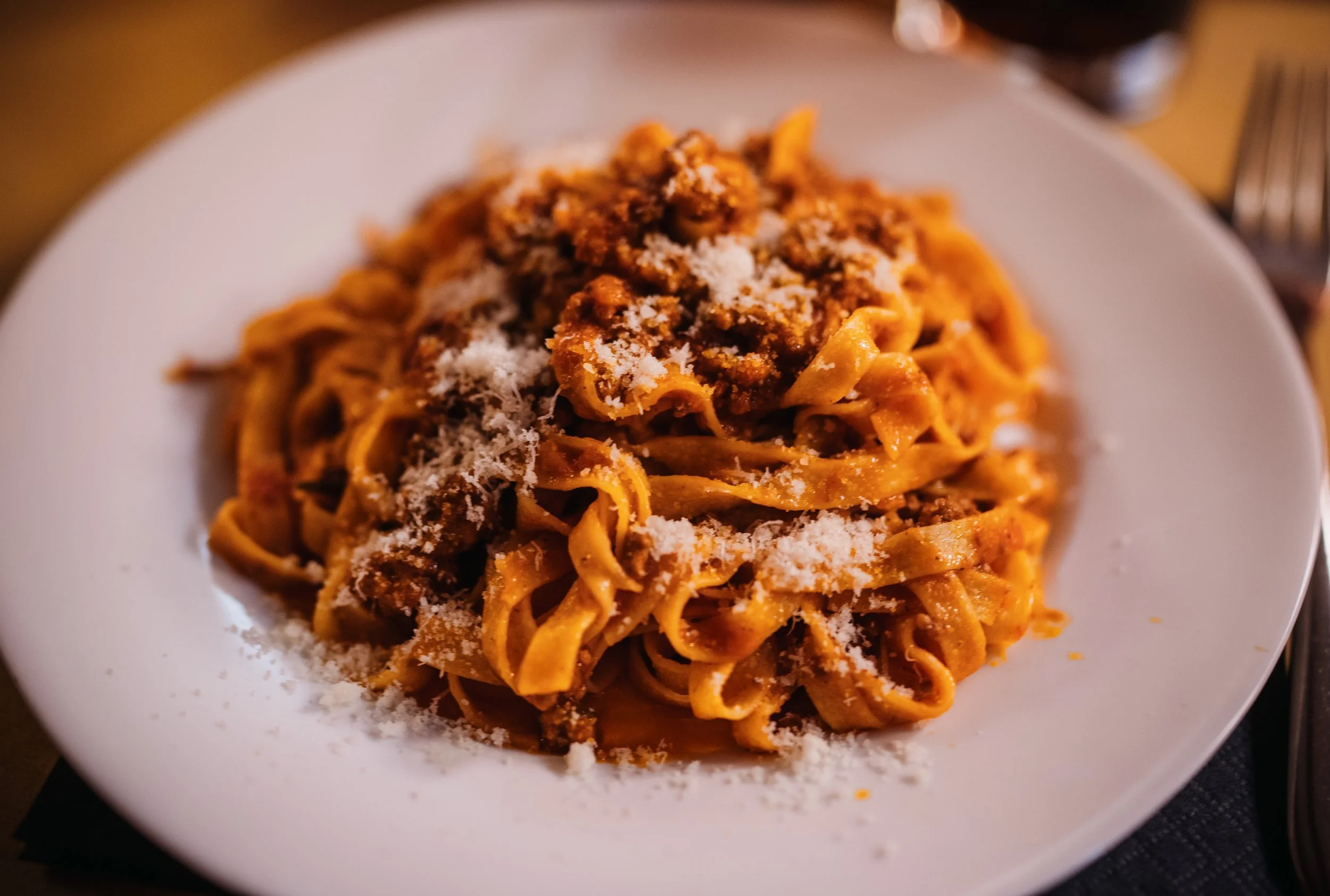Plate of Italian pasta with meat sauce and grated cheese.