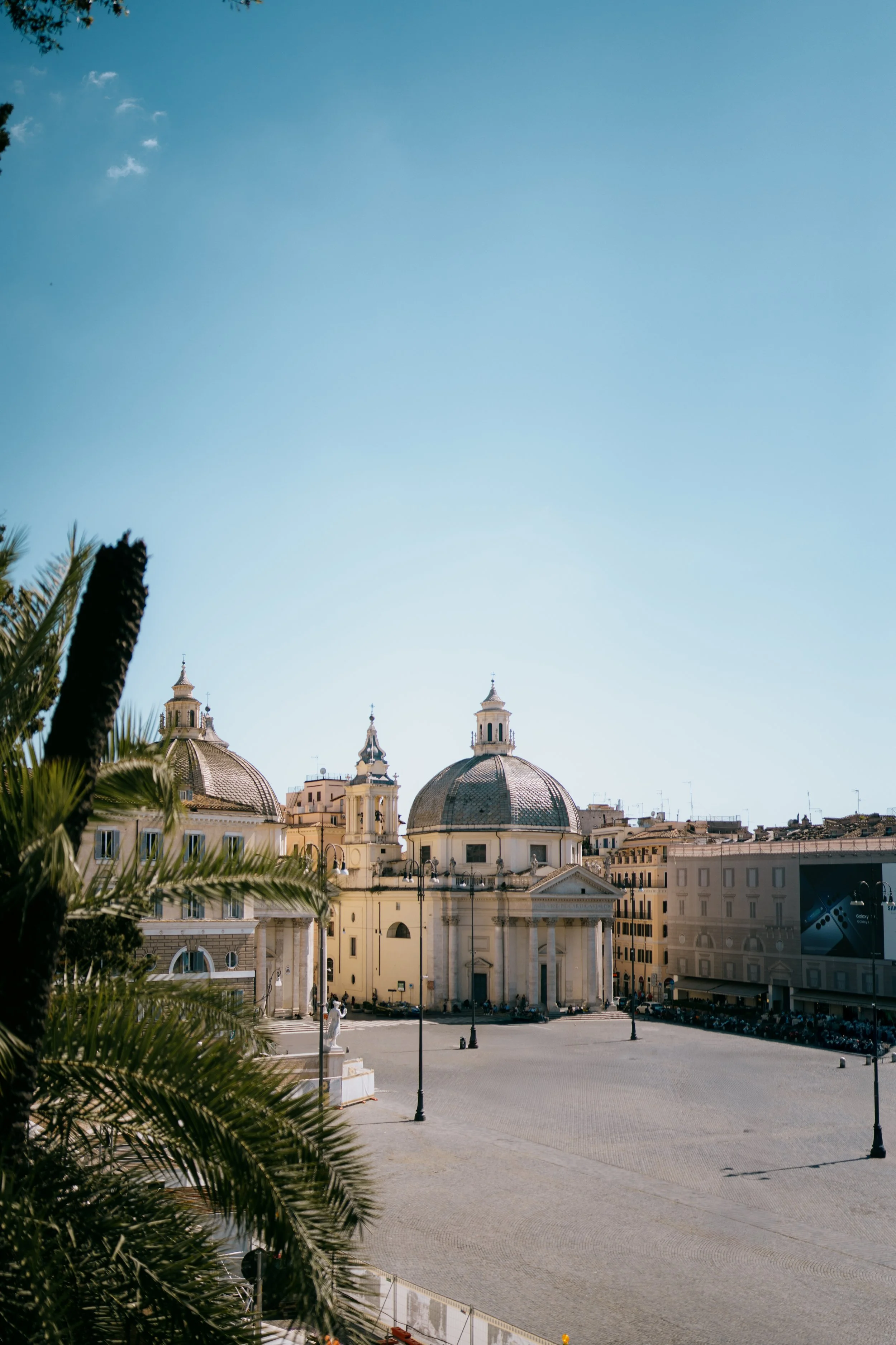 Historical city square with prominent domed church structures and ancient architecture under clear blue sky.