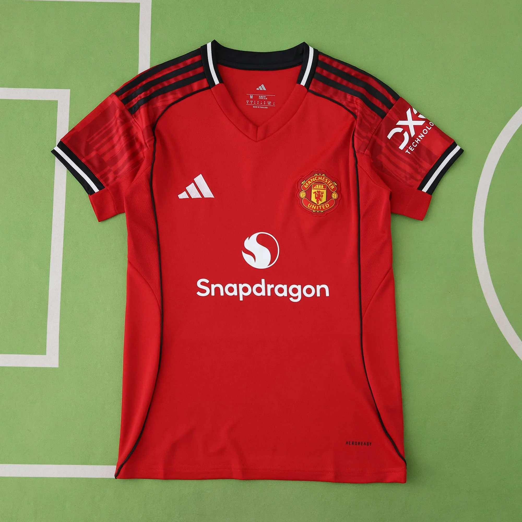 Red Manchester United soccer jersey with black and white accents, featuring the Adidas logo, Snapdragon sponsorship, and Manchester United crest, laid flat on a green surface.