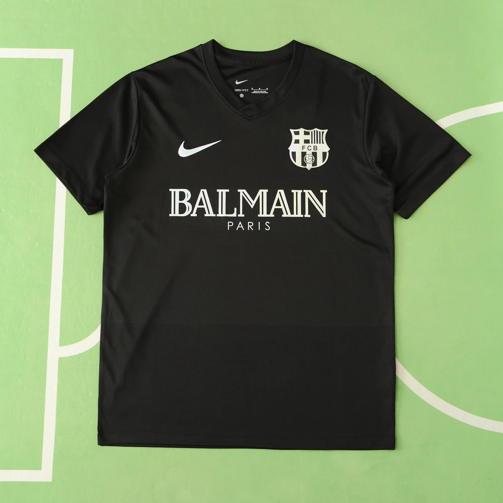 Black soccer jersey with white sponsor logo, Nike swoosh, FCB crest, and green background.