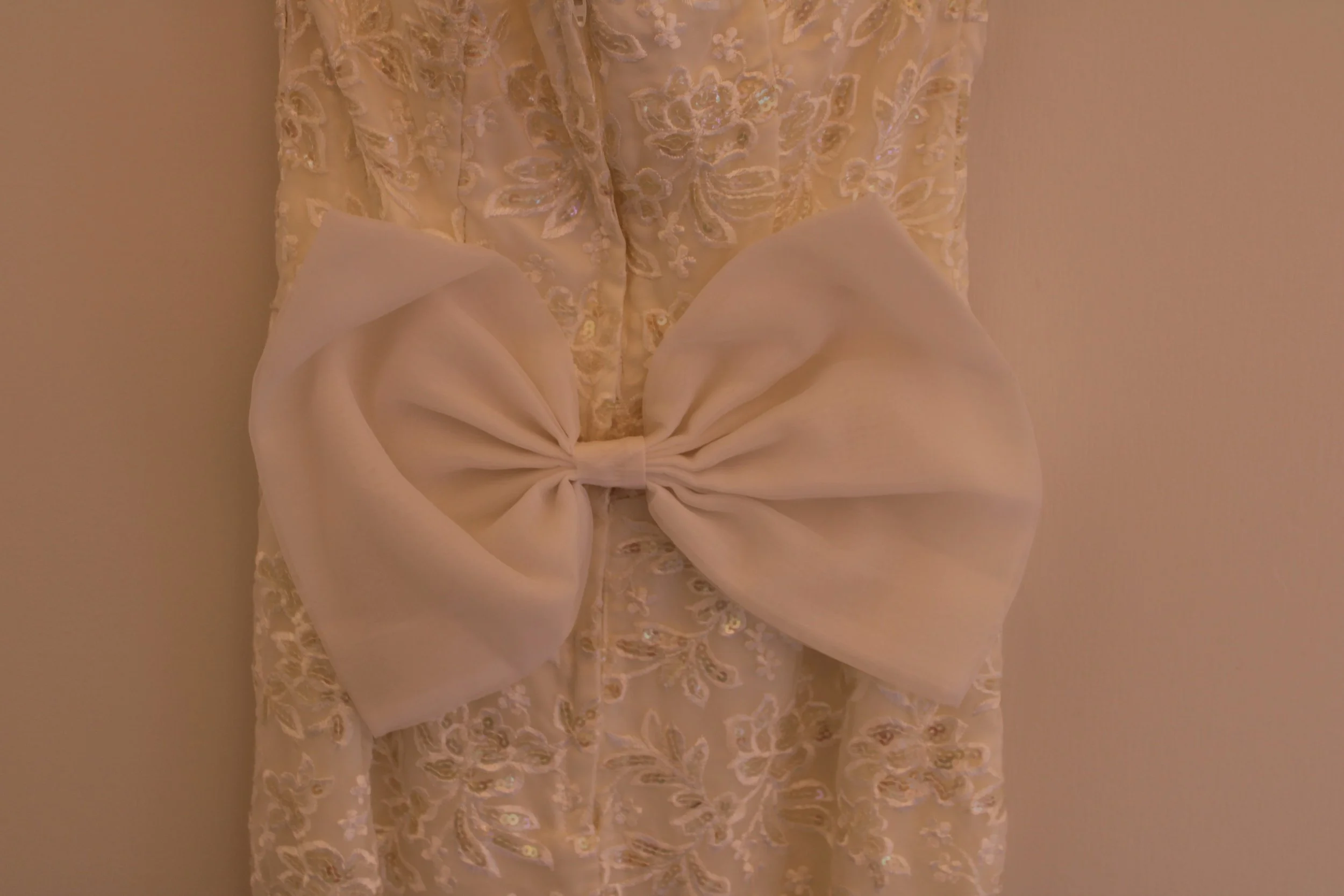 A cream-colored dress with intricate embroidery and a large, fabric bow at the waist.