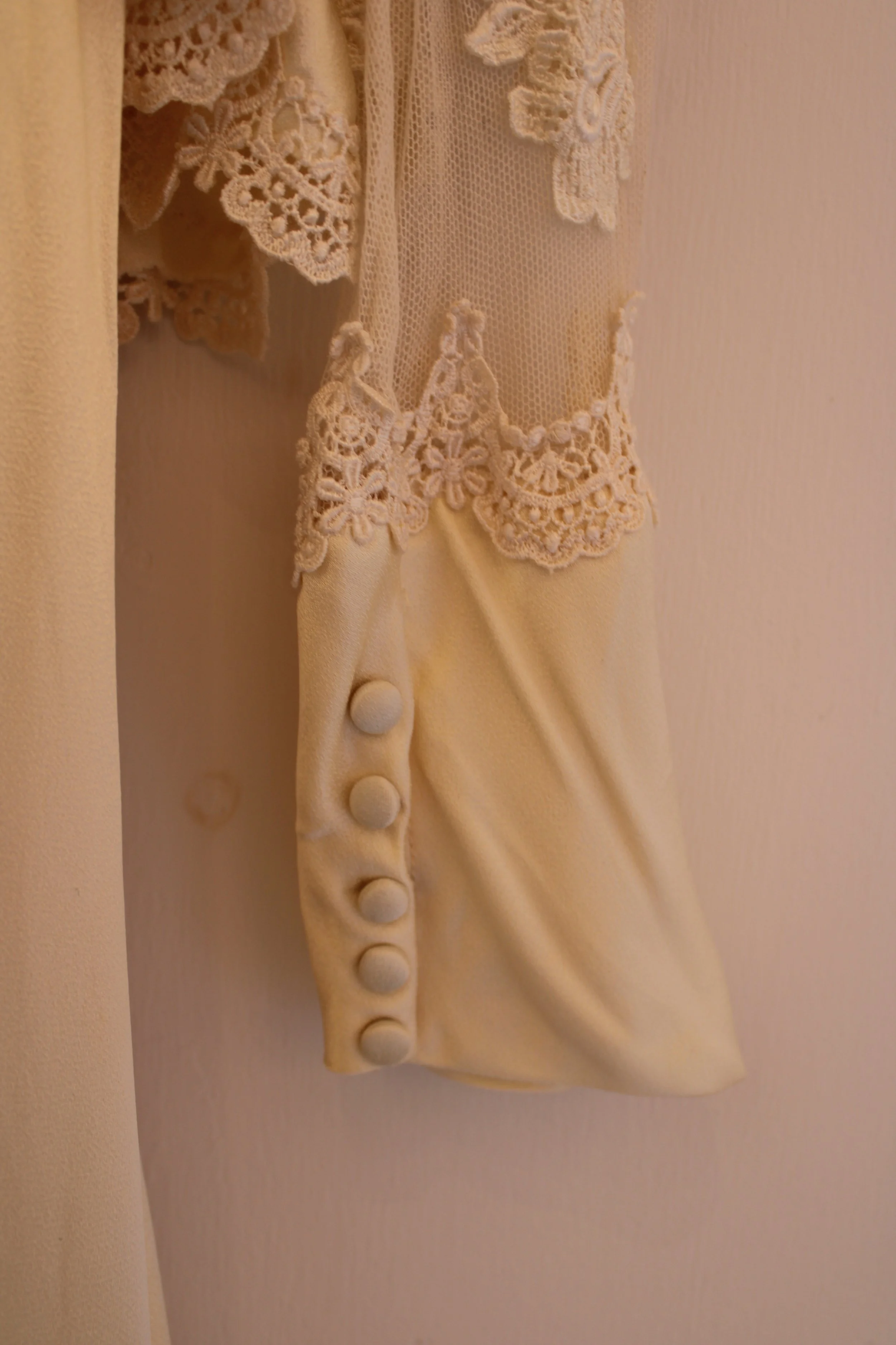Close-up of a vintage cream-colored dress with lace details and buttons on the sleeve.