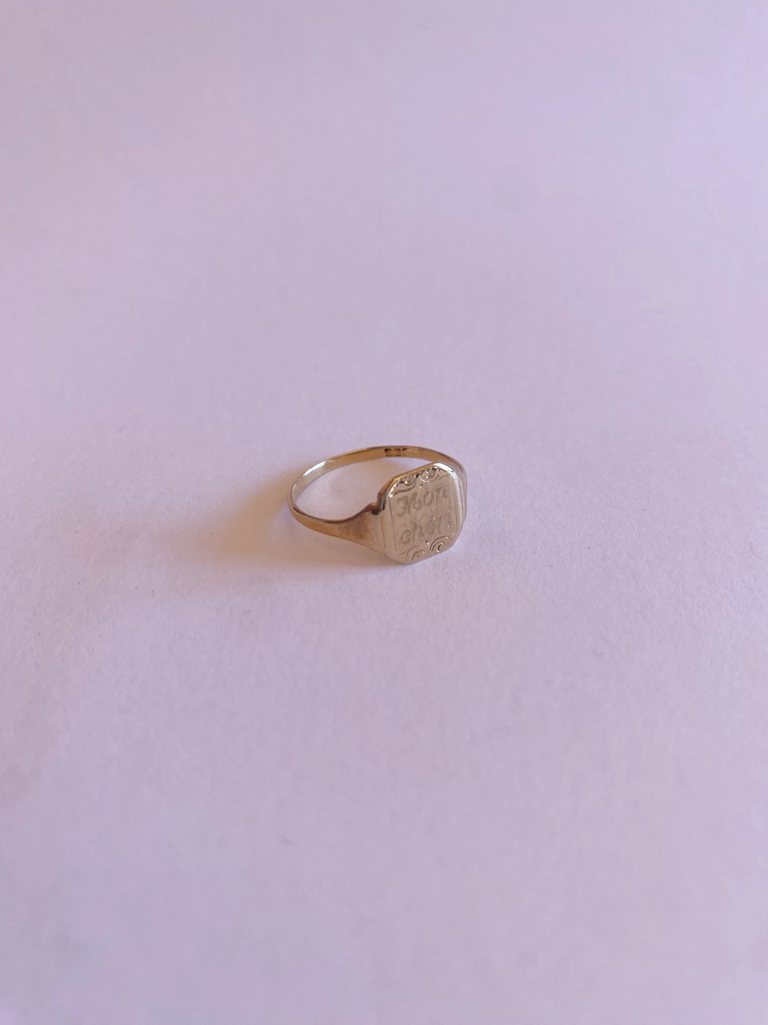 Silver ring with engraved design on a pale pink background.