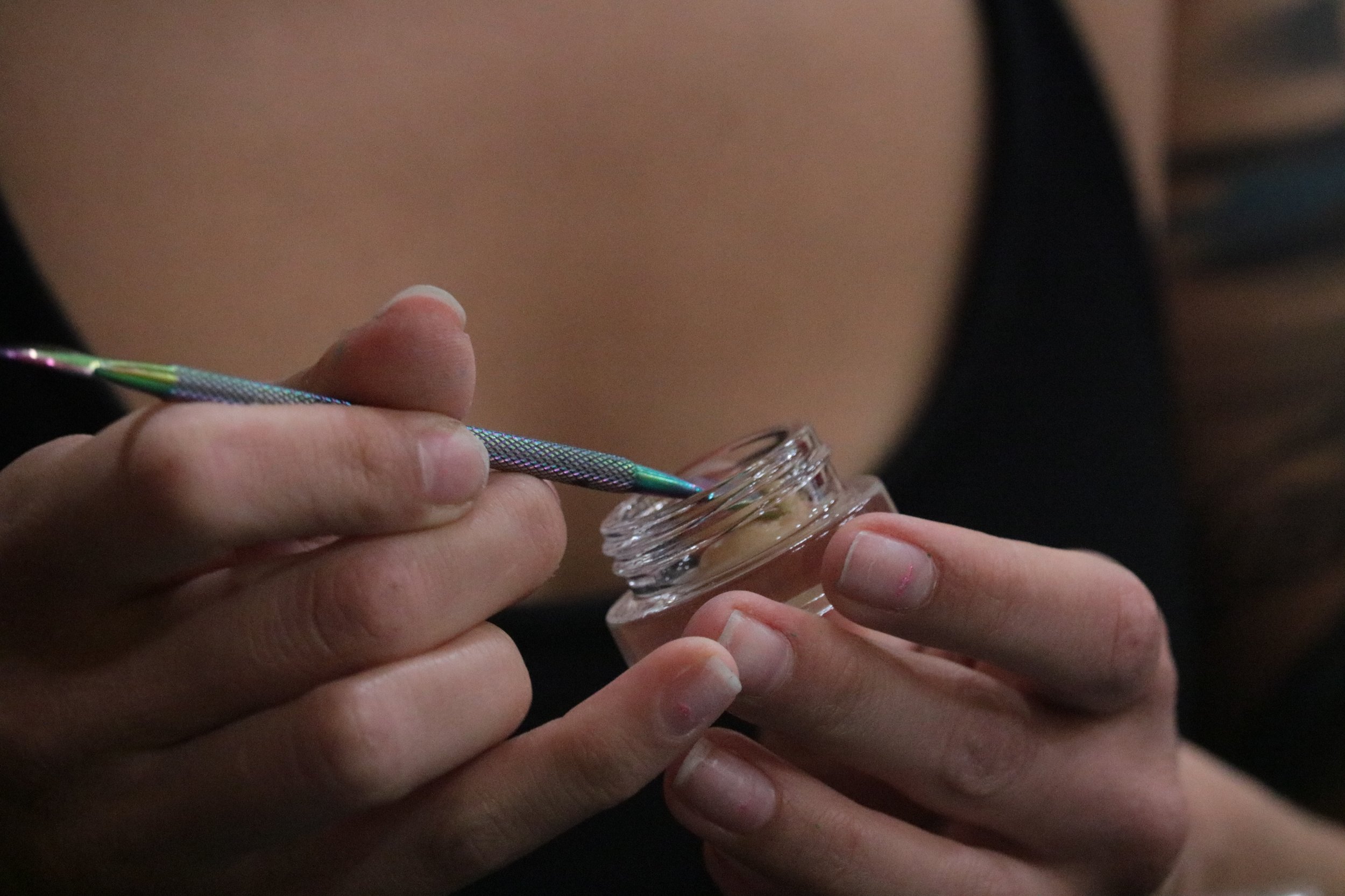 Close-up of a person's hands holding a jar of rosin and taking a dab 