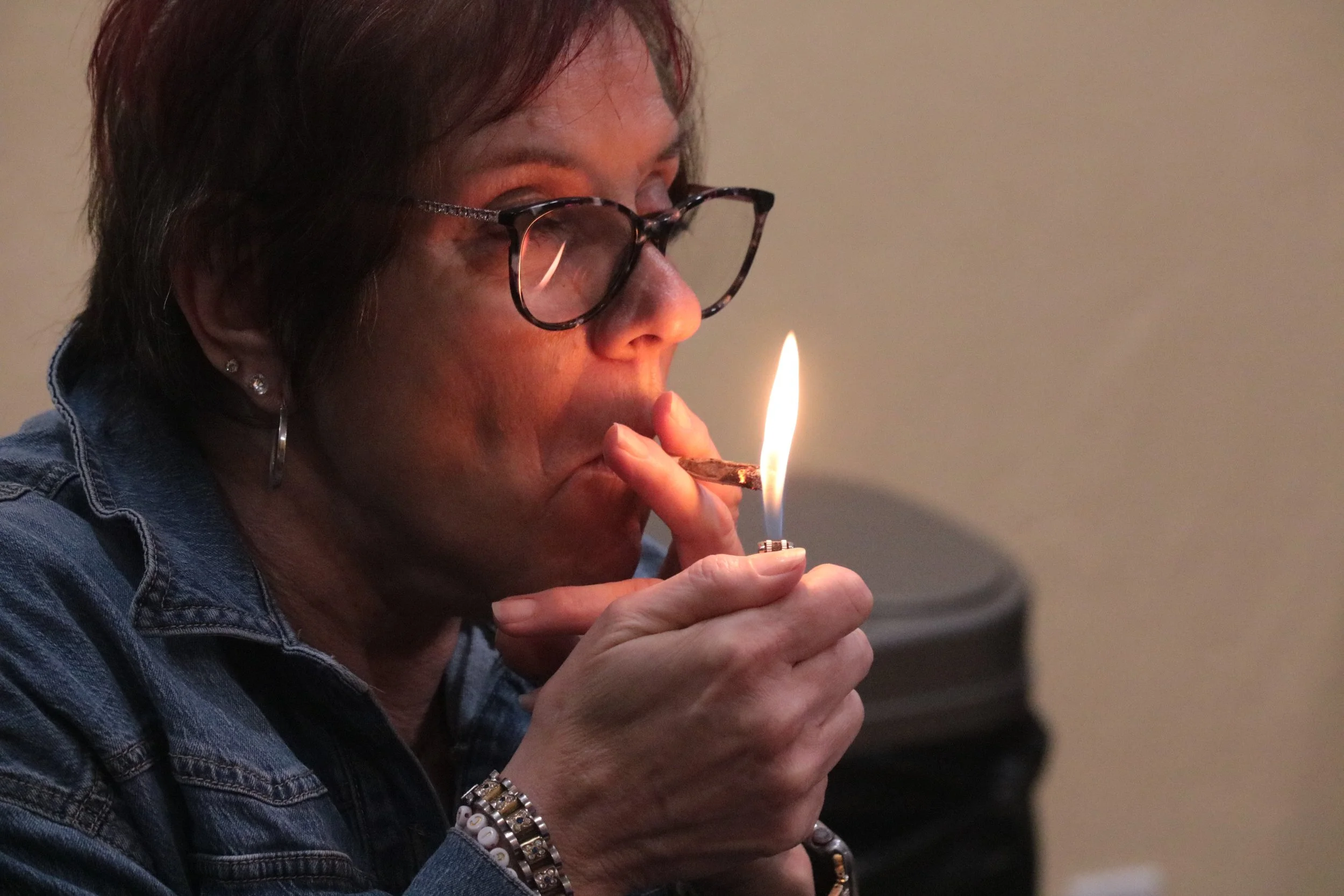 A woman with dark hair, glasses, and earrings is lighting a joint from Abundant Organics  for puffNpaint 
